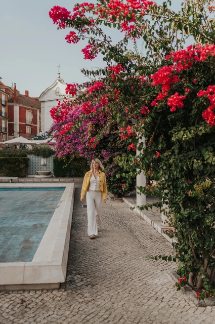 The woman walking beside bright flowers and a tiled pool at Santa Luzia during her solo photoshoot in Lisbon.