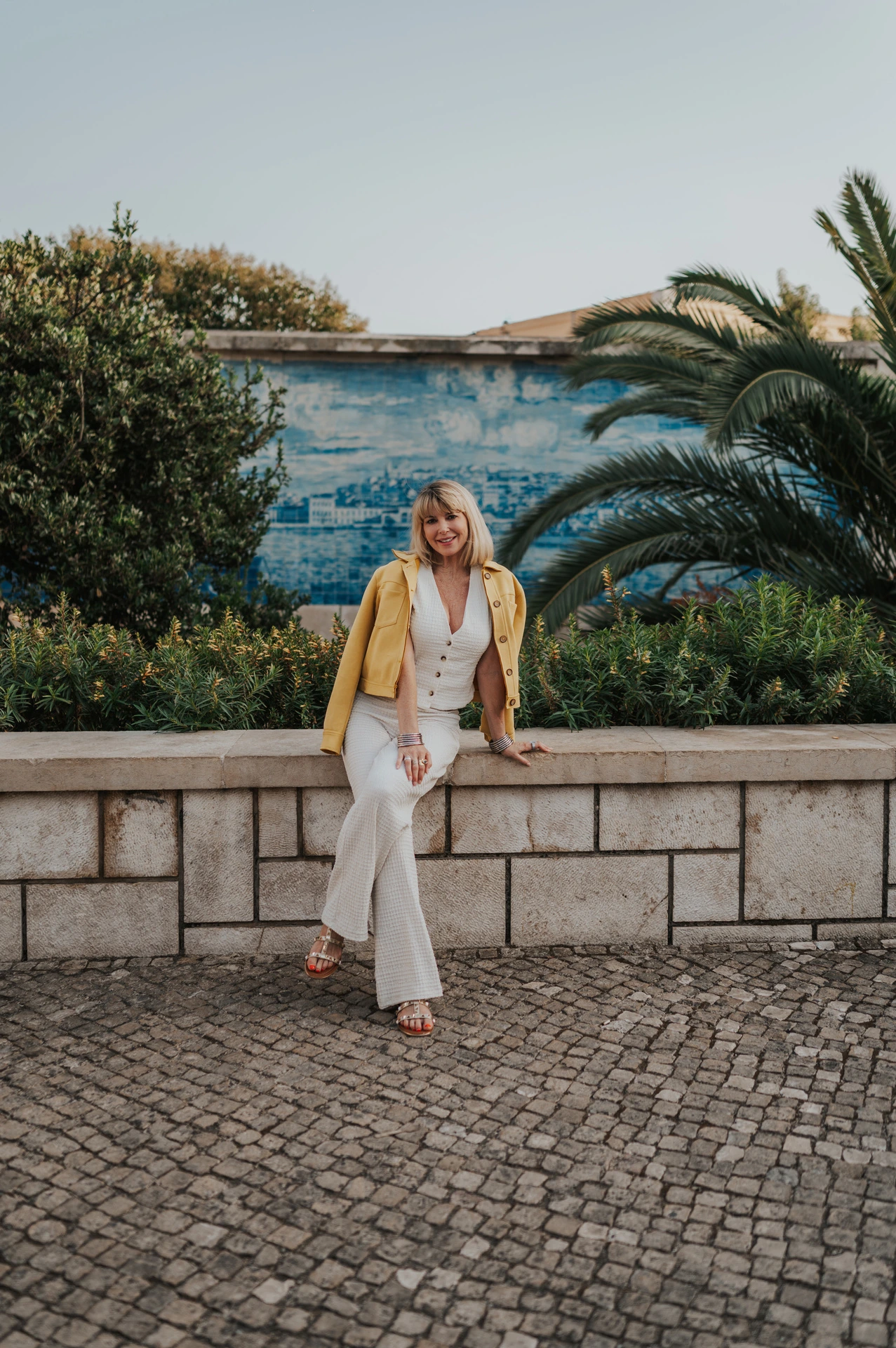 The woman seated on the garden wall with one leg crossed and blue tiles behind her at Santa Luzia during her solo photoshoot in Lisbon.