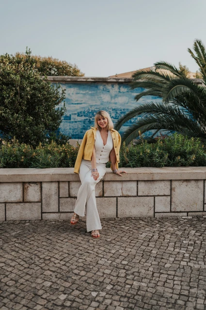 The woman seated on the garden wall with one leg crossed and blue tiles behind her at Santa Luzia during her solo photoshoot in Lisbon.