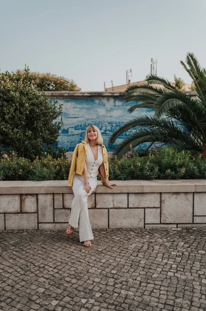 A seated smile at Santa Luzia | Lisbon solo photoshoot The woman smiling while seated on the low garden wall beneath the palms at Santa Luzia during her solo photoshoot in Lisbon.