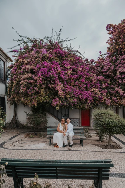 A seated portrait beneath the flowers | Lisbon couple photoshoot The couple seated together on a garden bench beneath flowering branches during their couple photoshoot in Lisbon.