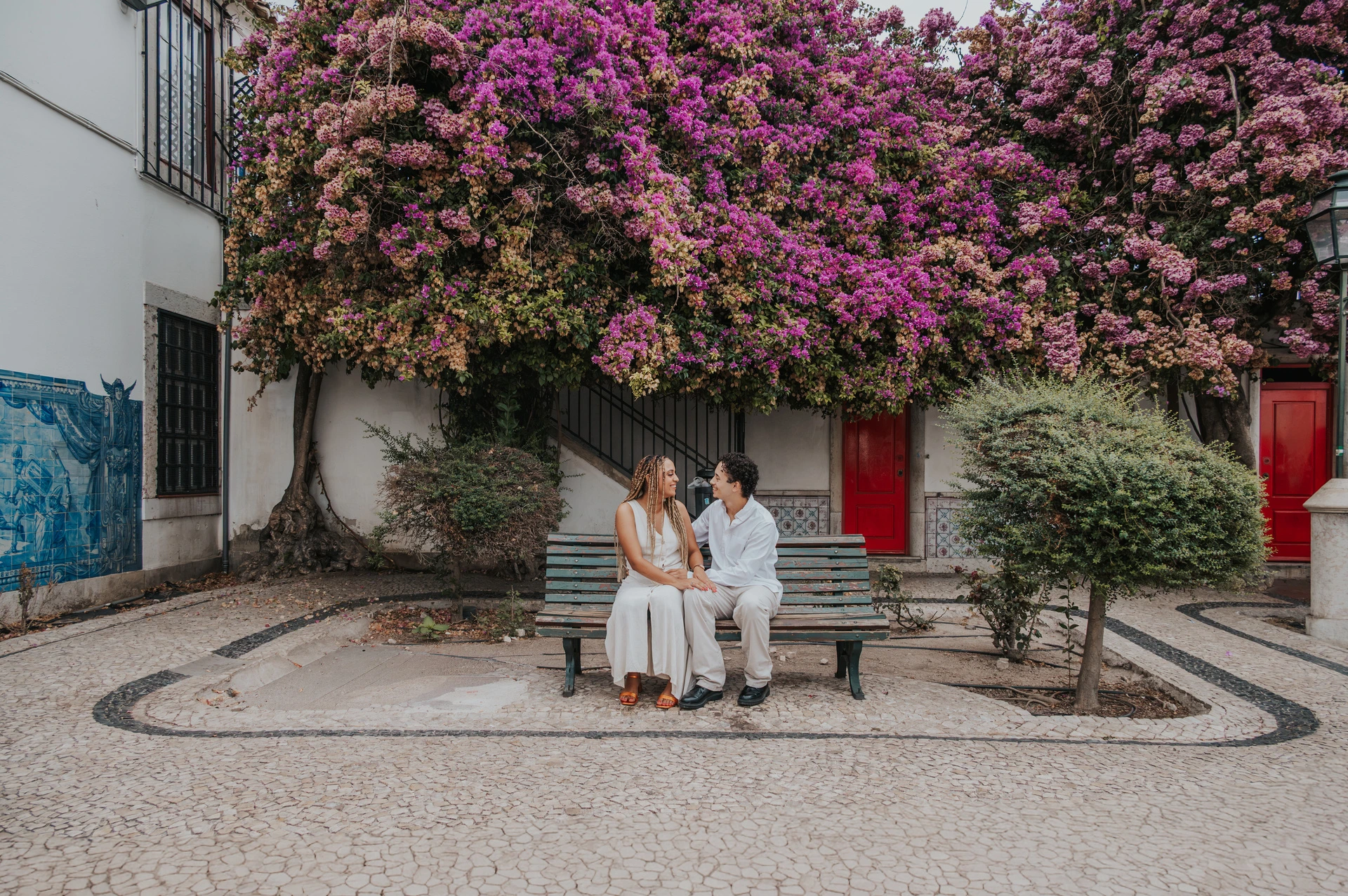 The couple seated together on a garden bench beneath flowering branches during their couple photoshoot in Lisbon.