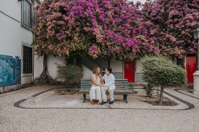 The couple seated together on a garden bench beneath flowering branches during their couple photoshoot in Lisbon.
