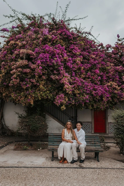 A seated portrait beneath the flowers | Lisbon couple photoshoot The couple seated together on a garden bench beneath flowering branches during their couple photoshoot in Lisbon.
