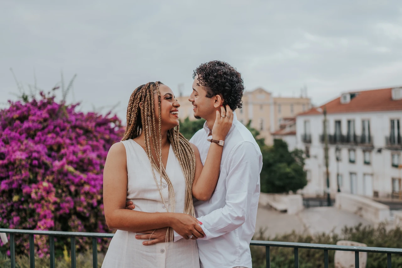 A shared smile beside the flowers | Lisbon couple photoshoot The couple smiling at each other beside the garden railing and purple flowers during their couple photoshoot in Lisbon.