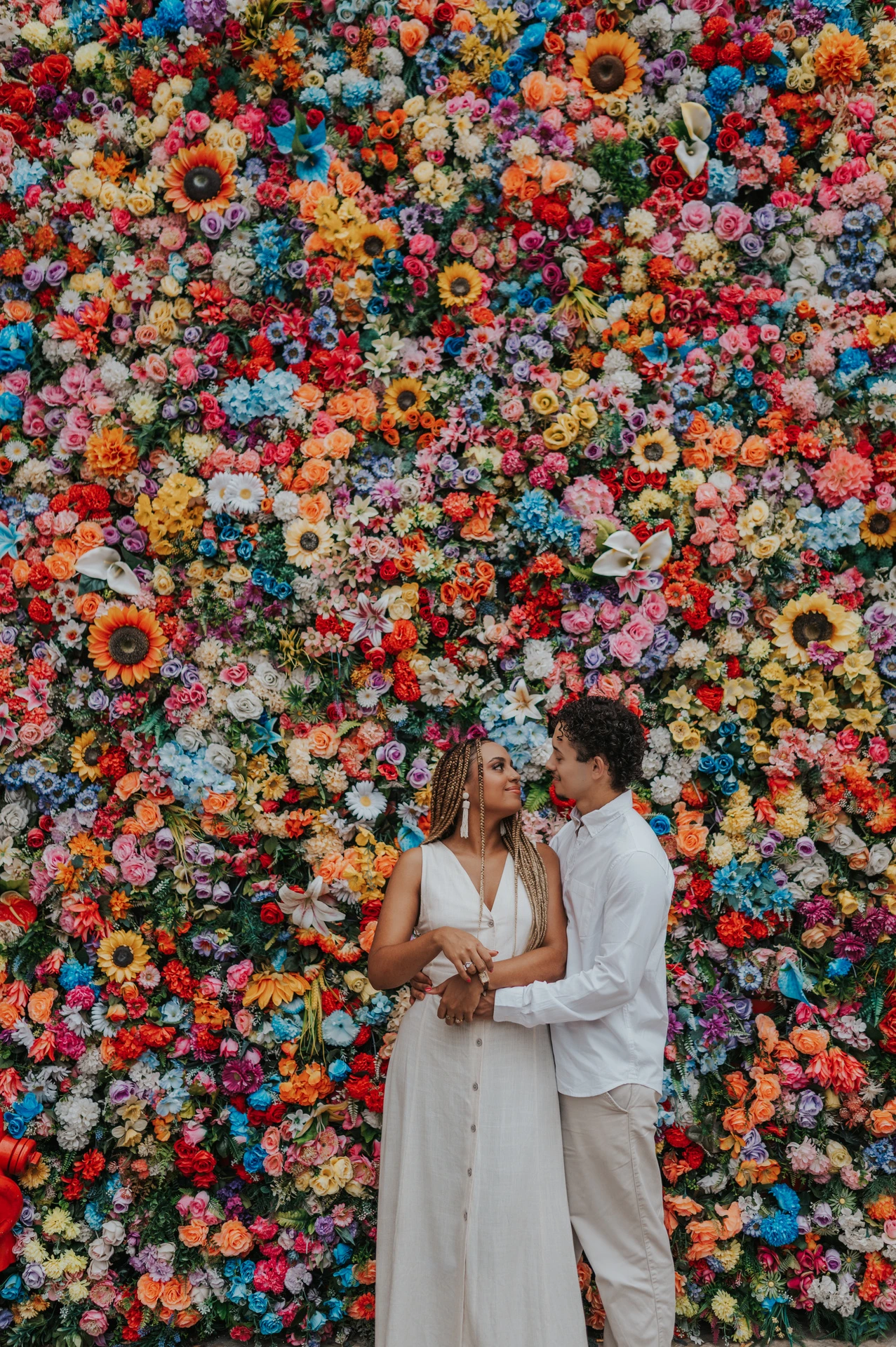 The couple standing close together in front of a wall covered in colourful flowers during their couple photoshoot in Lisbon.