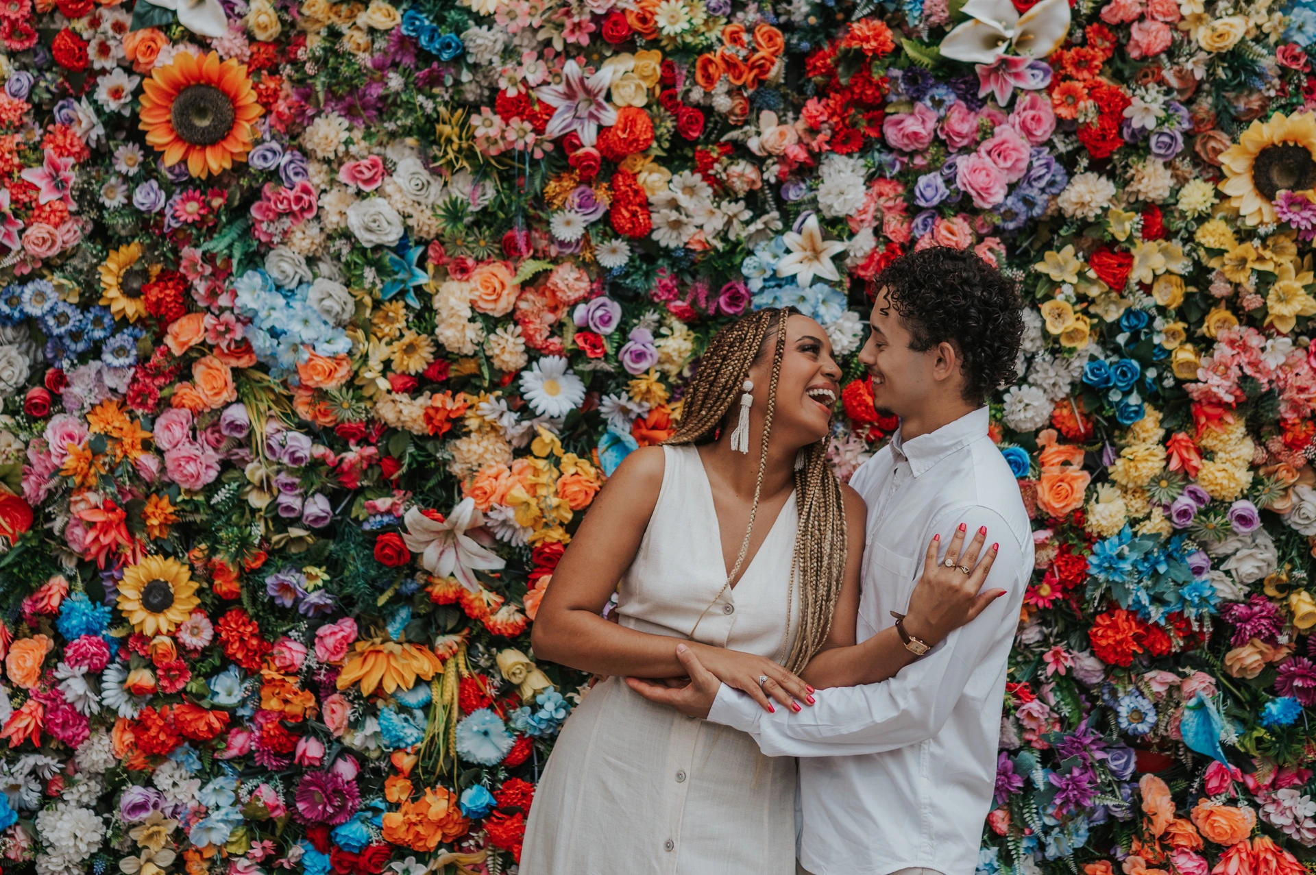 The couple standing close together in front of a wall covered in colourful flowers during their couple photoshoot in Lisbon.