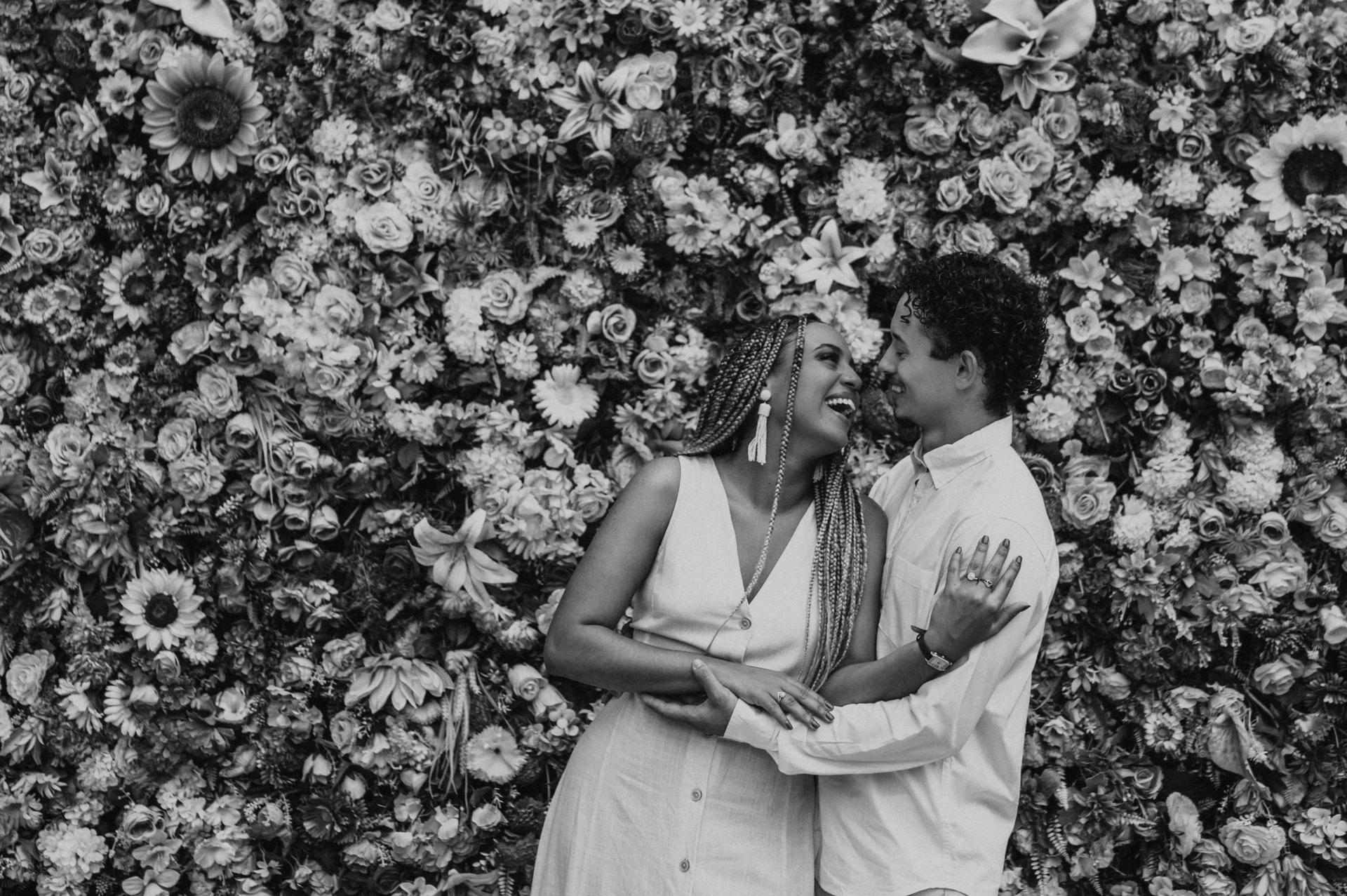 Black-and-white photograph: the couple standing close together in front of a wall covered in colourful flowers during their couple photoshoot in Lisbon.