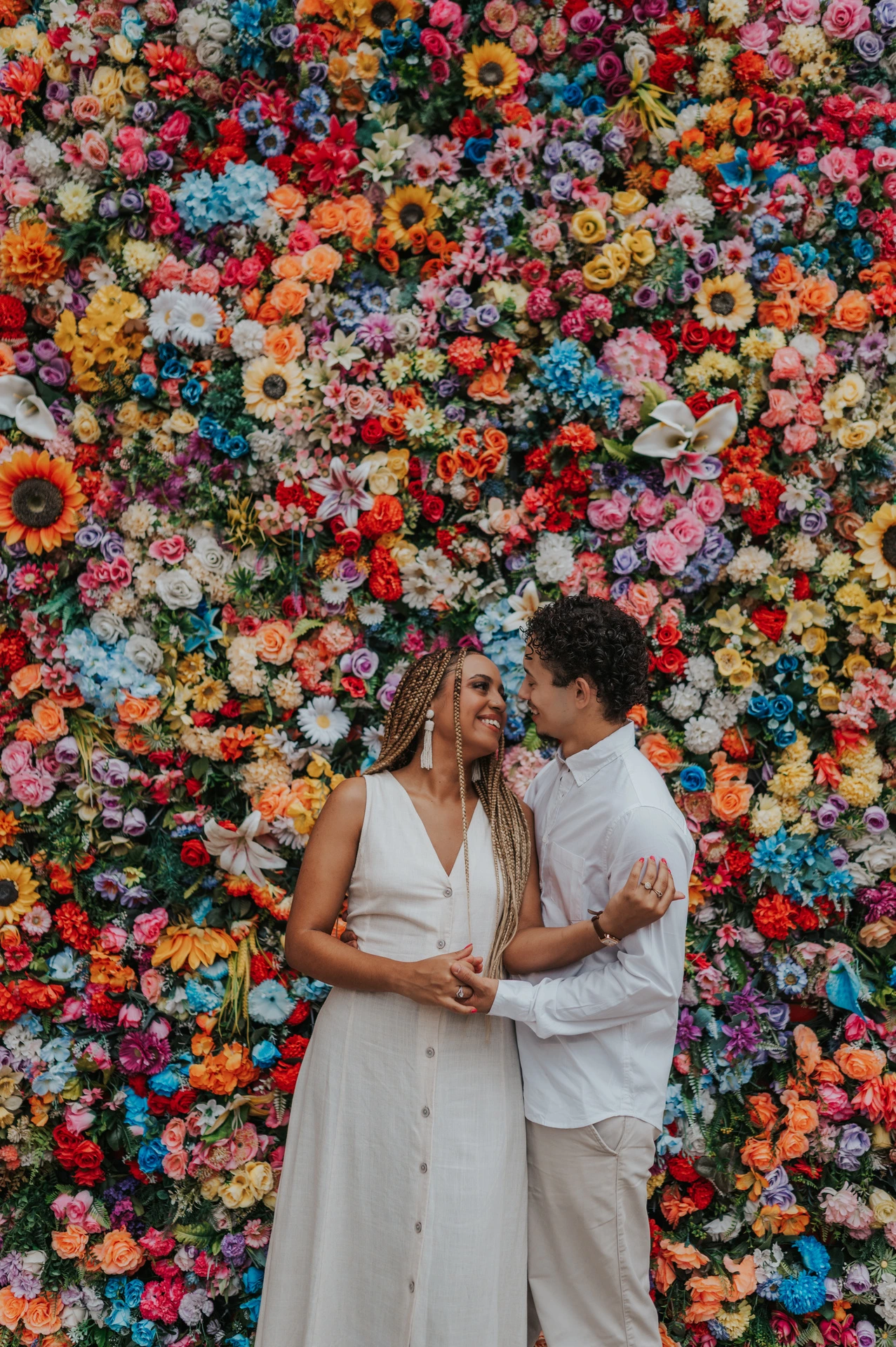 The couple standing close together in front of a wall covered in colourful flowers during their couple photoshoot in Lisbon.