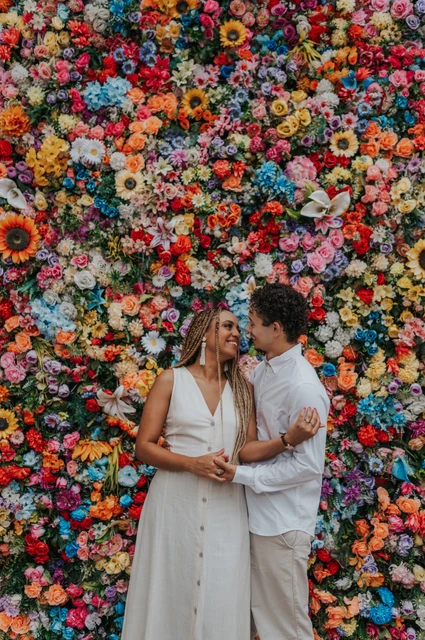 Together against the colourful flower wall | Lisbon couple photoshoot The couple standing close together in front of a wall covered in colourful flowers during their couple photoshoot in Lisbon.