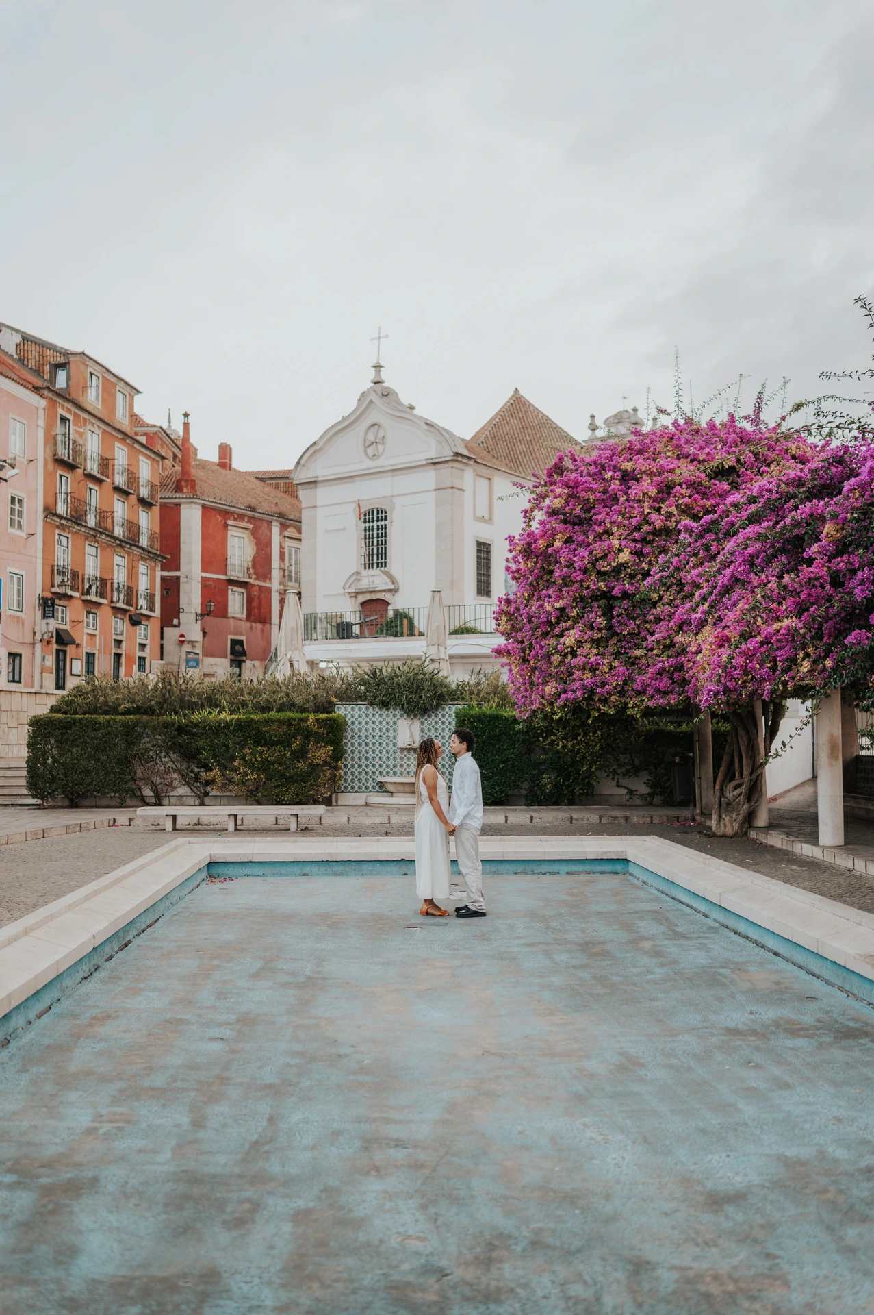 The couple embracing beside the shallow garden pool and flowering branches during their couple photoshoot in Lisbon.