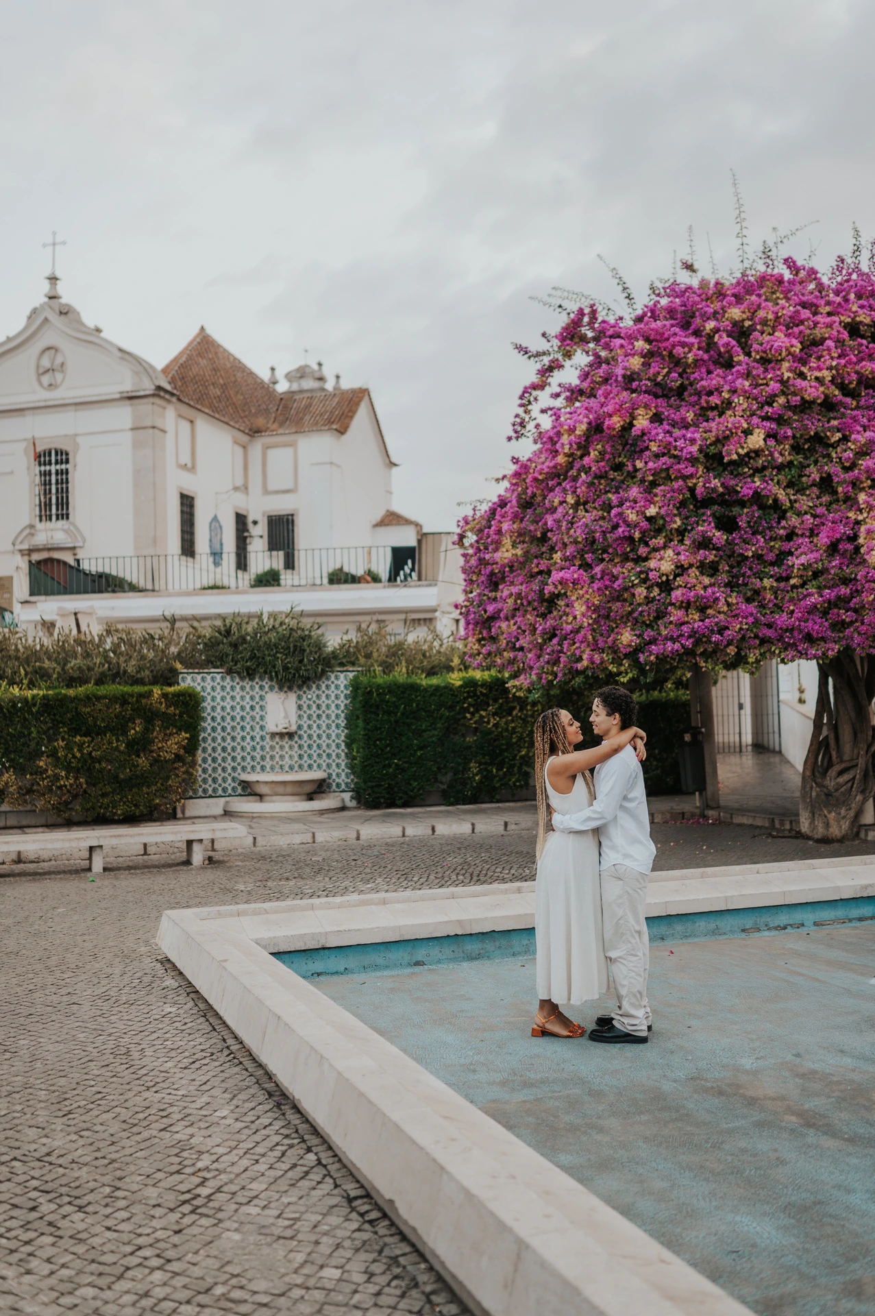 The couple embracing beside the shallow garden pool and flowering branches during their couple photoshoot in Lisbon.