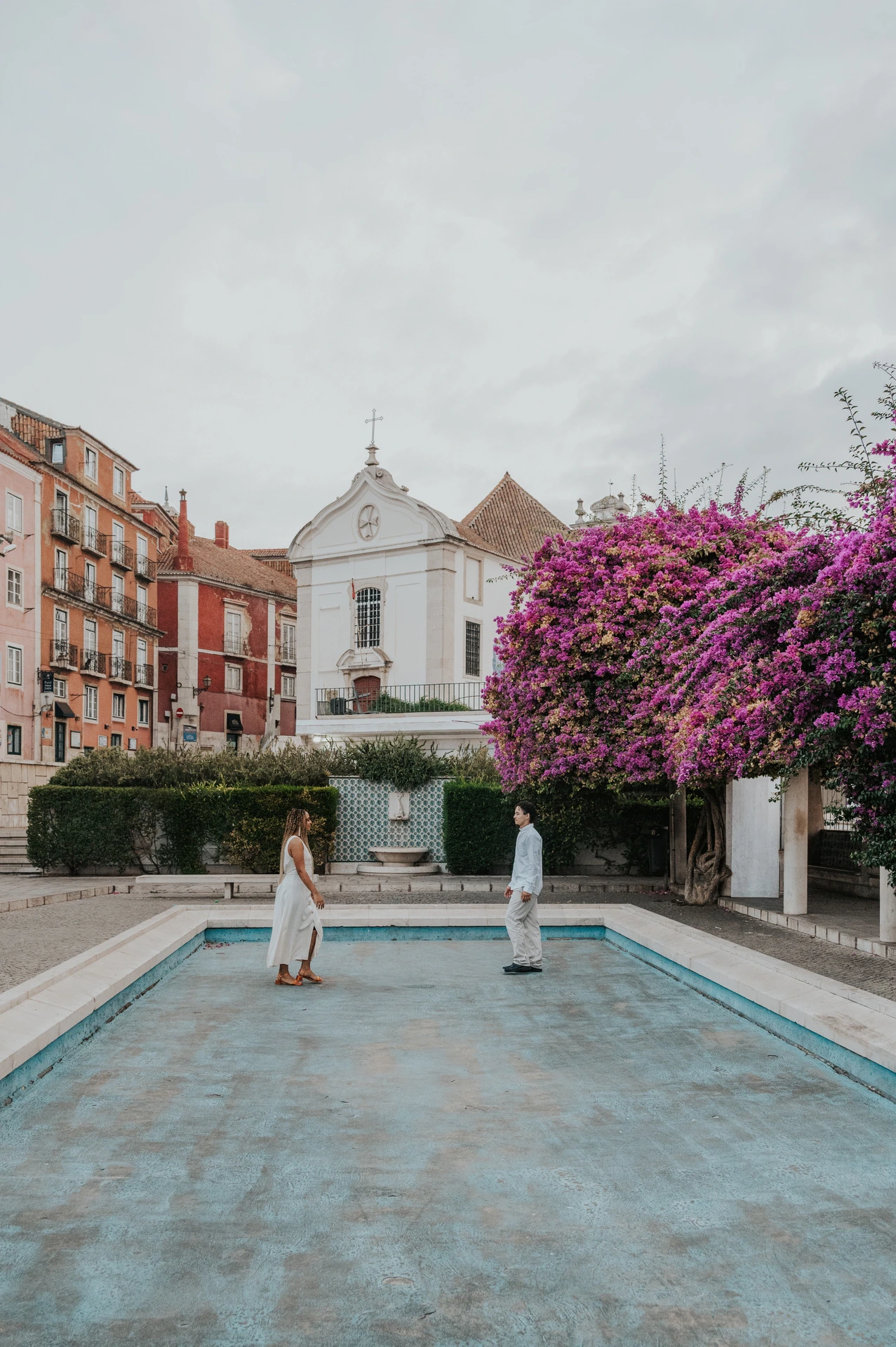 The couple facing each other across the paved edge of the garden pool during their couple photoshoot in Lisbon.