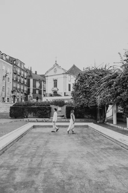 A hand-in-hand moment beside the garden pool in black and white | Lisbon couple photoshoot Black-and-white photograph: the couple facing each other across the paved edge of the garden pool during their couple photoshoot in Lisbon.