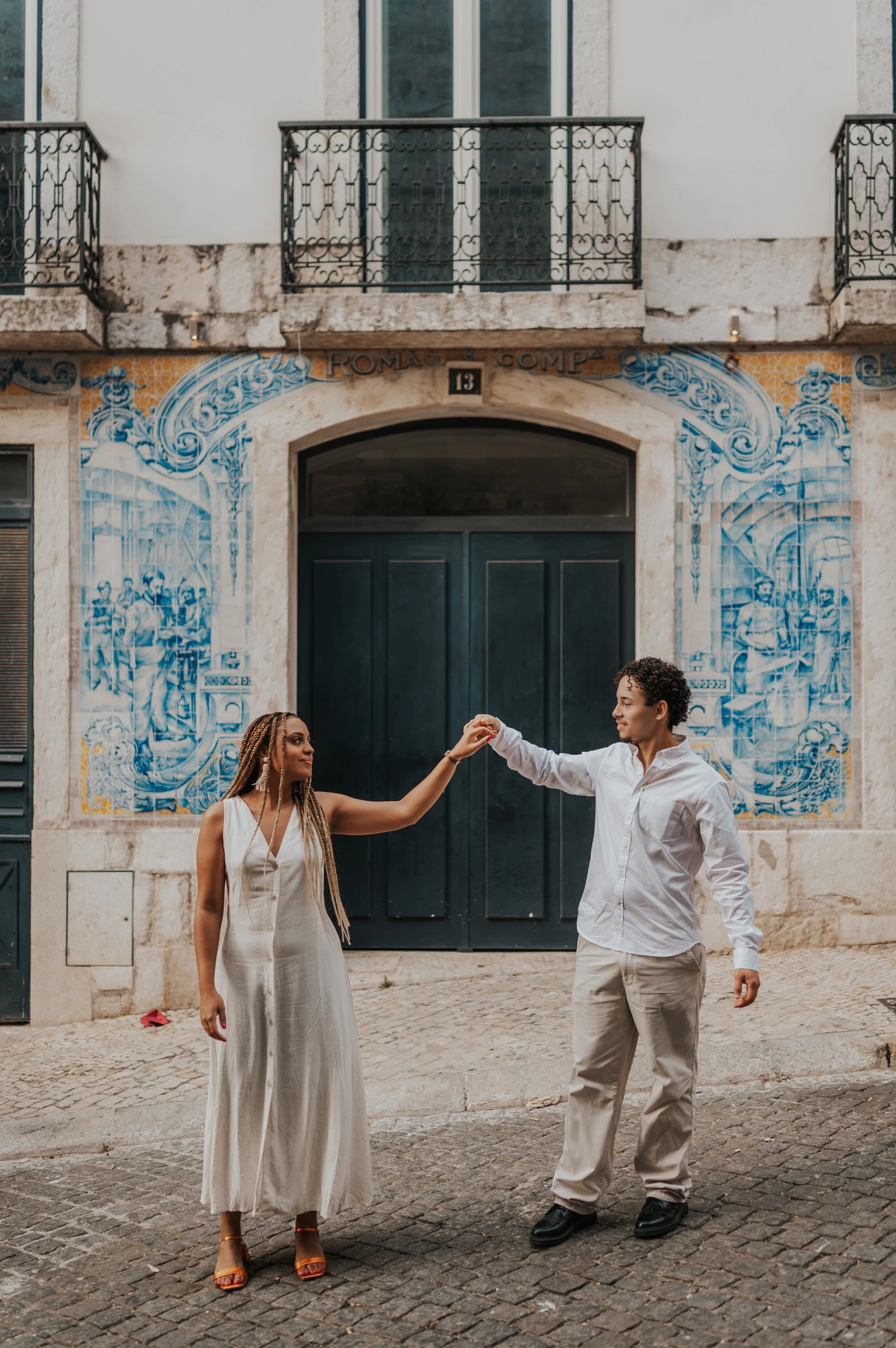 The couple raising their joined hands across the green doorway surrounded by blue tiles during their couple photoshoot in Lisbon.