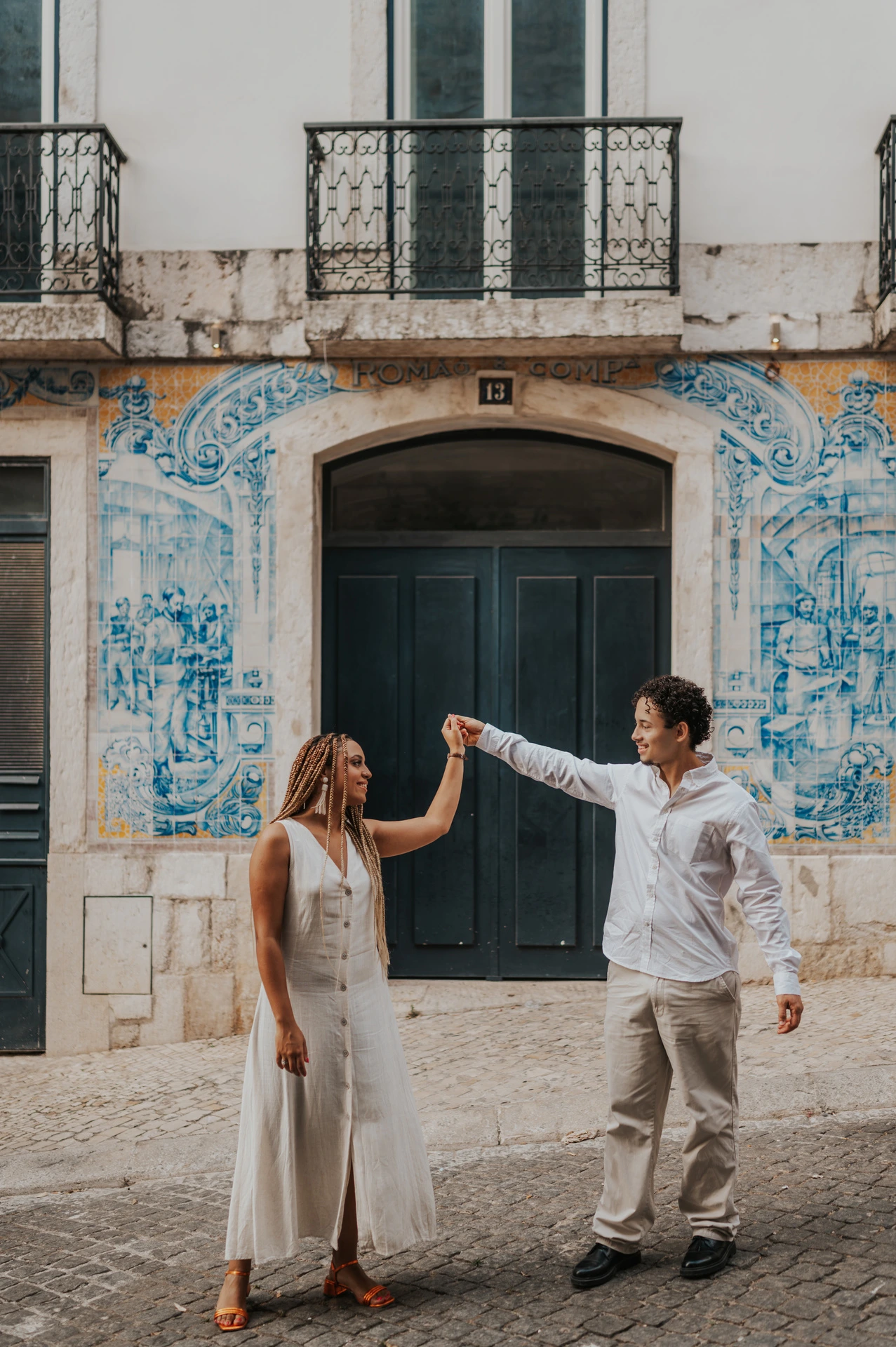 The couple raising their joined hands across the green doorway surrounded by blue tiles during their couple photoshoot in Lisbon.