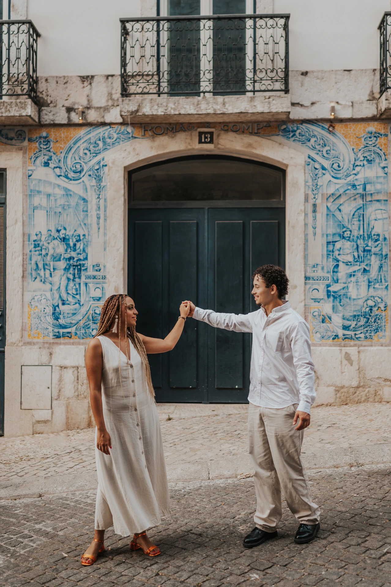 The couple raising their joined hands across the green doorway surrounded by blue tiles during their couple photoshoot in Lisbon.