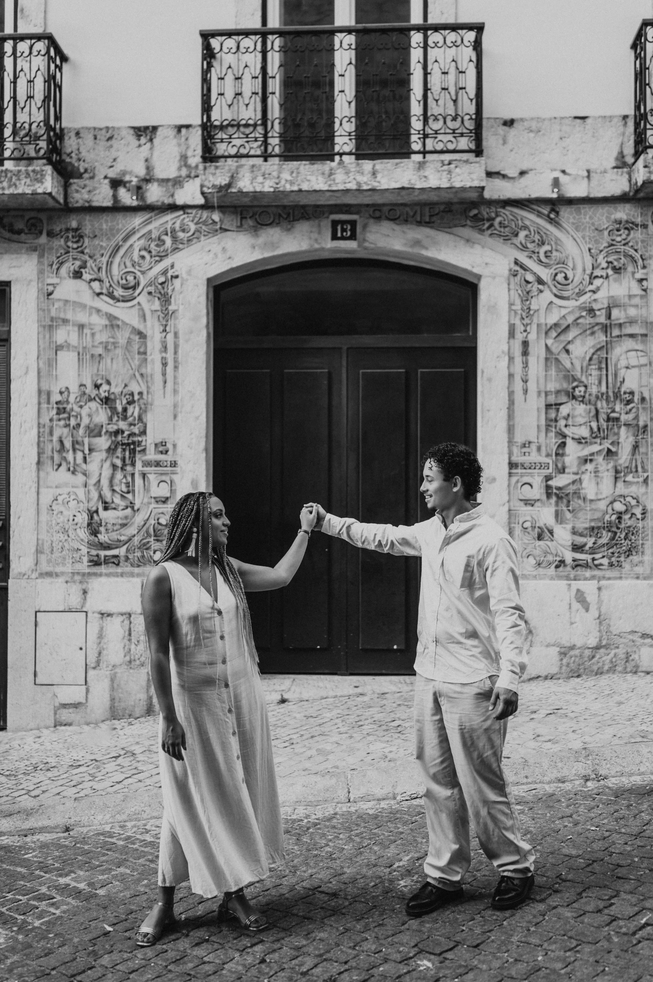 Black-and-white photograph: the couple raising their joined hands across the green doorway surrounded by blue tiles during their couple photoshoot in Lisbon.