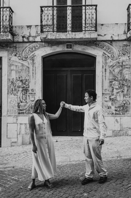 A hand-in-hand turn at the green door in black and white | Lisbon couple photoshoot Black-and-white photograph: the couple raising their joined hands across the green doorway surrounded by blue tiles during their couple photoshoot in Lisbon.
