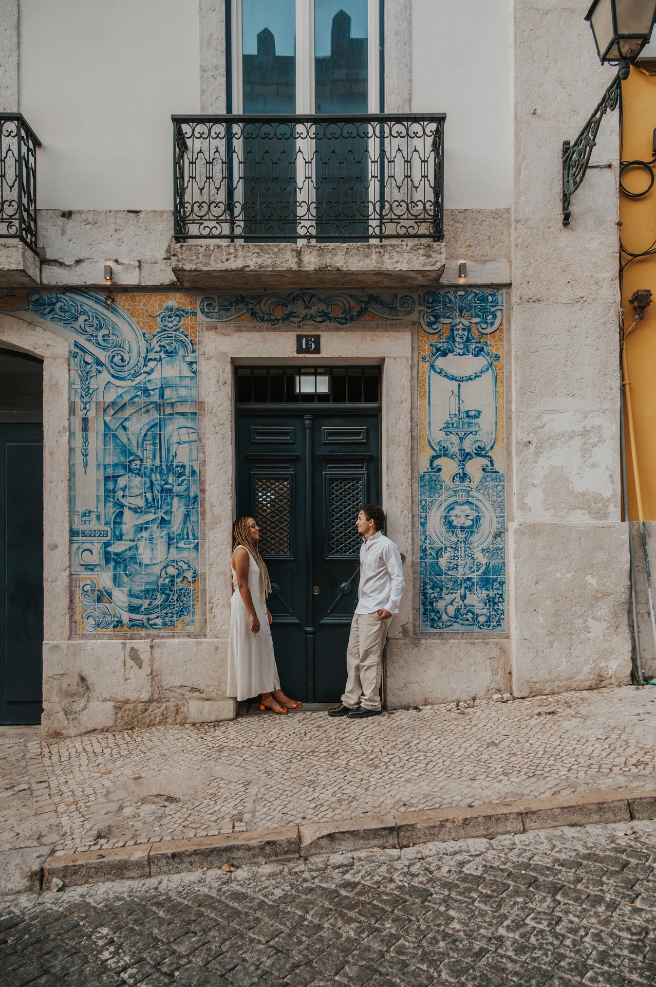 The couple standing on either side of a green doorway framed by blue Portuguese tiles during their couple photoshoot in Lisbon.