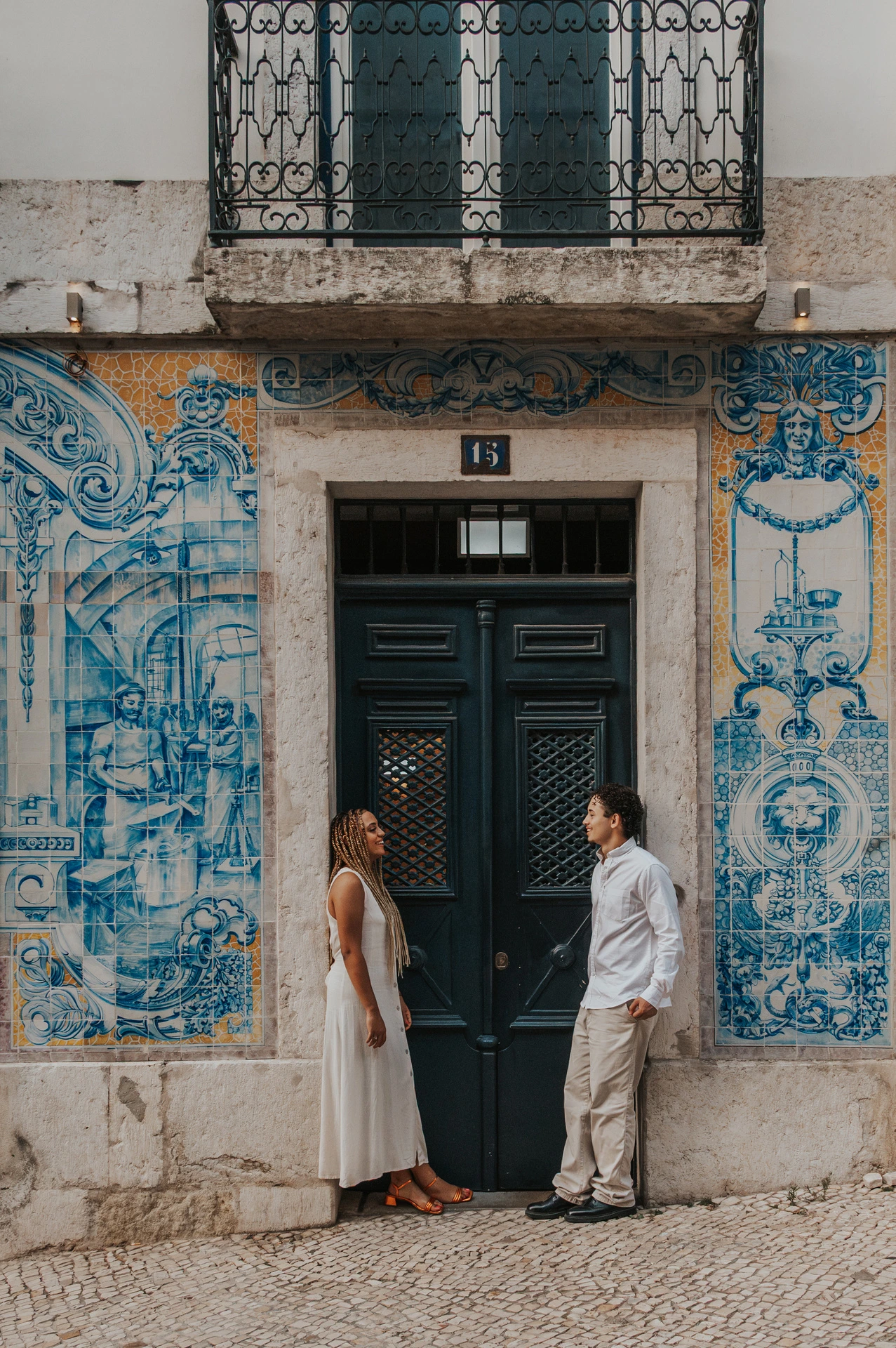 The couple standing on either side of a green doorway framed by blue Portuguese tiles during their couple photoshoot in Lisbon.