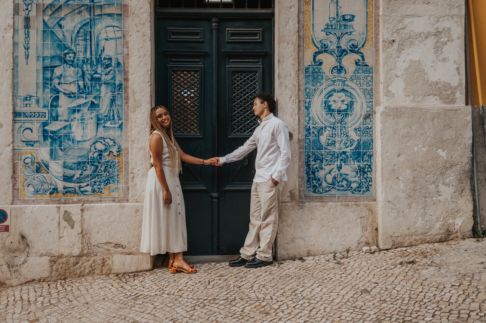 The couple standing on either side of a green doorway framed by blue Portuguese tiles during their couple photoshoot in Lisbon.