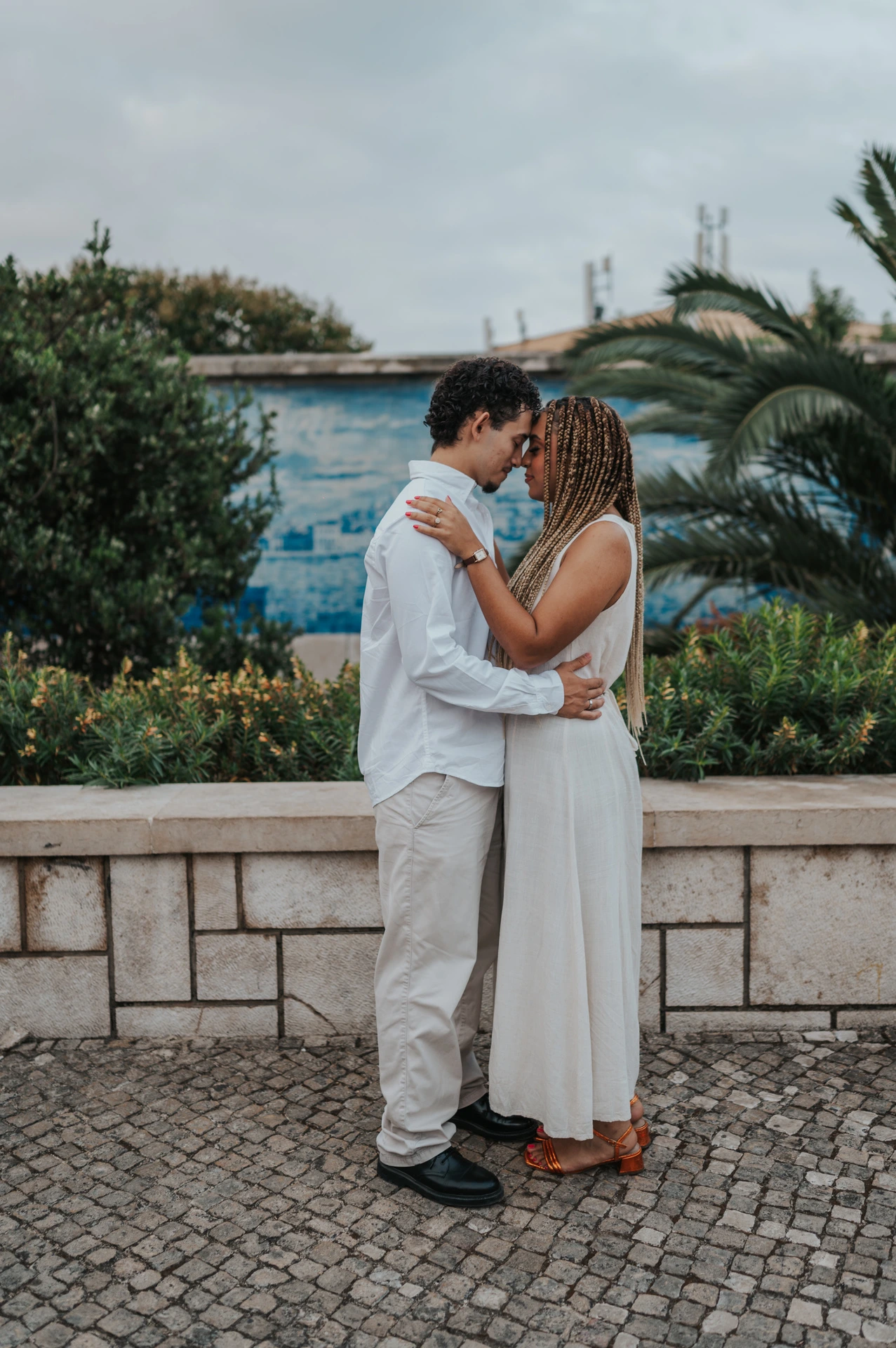 The couple holding each other close beside the palms and blue tiles during their couple photoshoot in Lisbon.