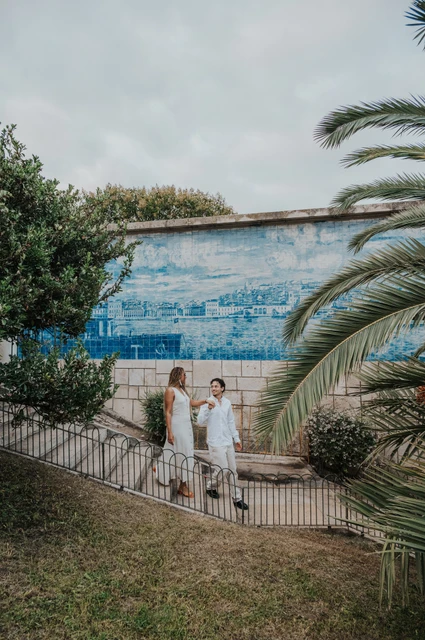 Together beside the palms and tiles | Lisbon couple photoshoot The couple holding hands beside a blue tile panel and palm leaves at the viewpoint during their couple photoshoot in Lisbon.