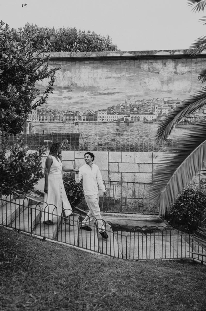 Together beside the palms and tiles in black and white | Lisbon couple photoshoot Black-and-white photograph: the couple holding hands beside a blue tile panel and palm leaves at the viewpoint during their couple photoshoot in Lisbon.