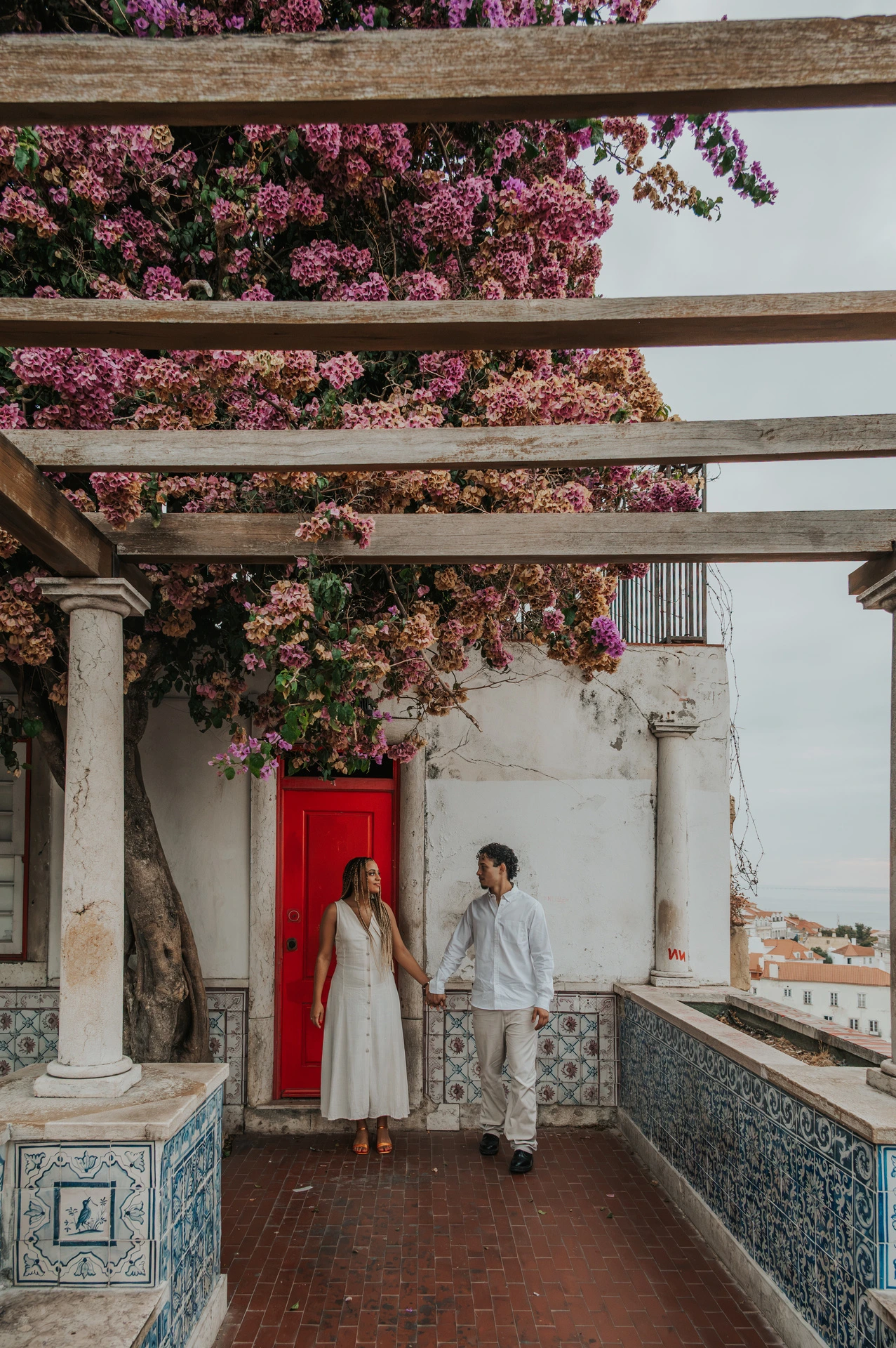 The couple holding hands beneath the garden pergola beside Portuguese tiles during their couple photoshoot in Lisbon.