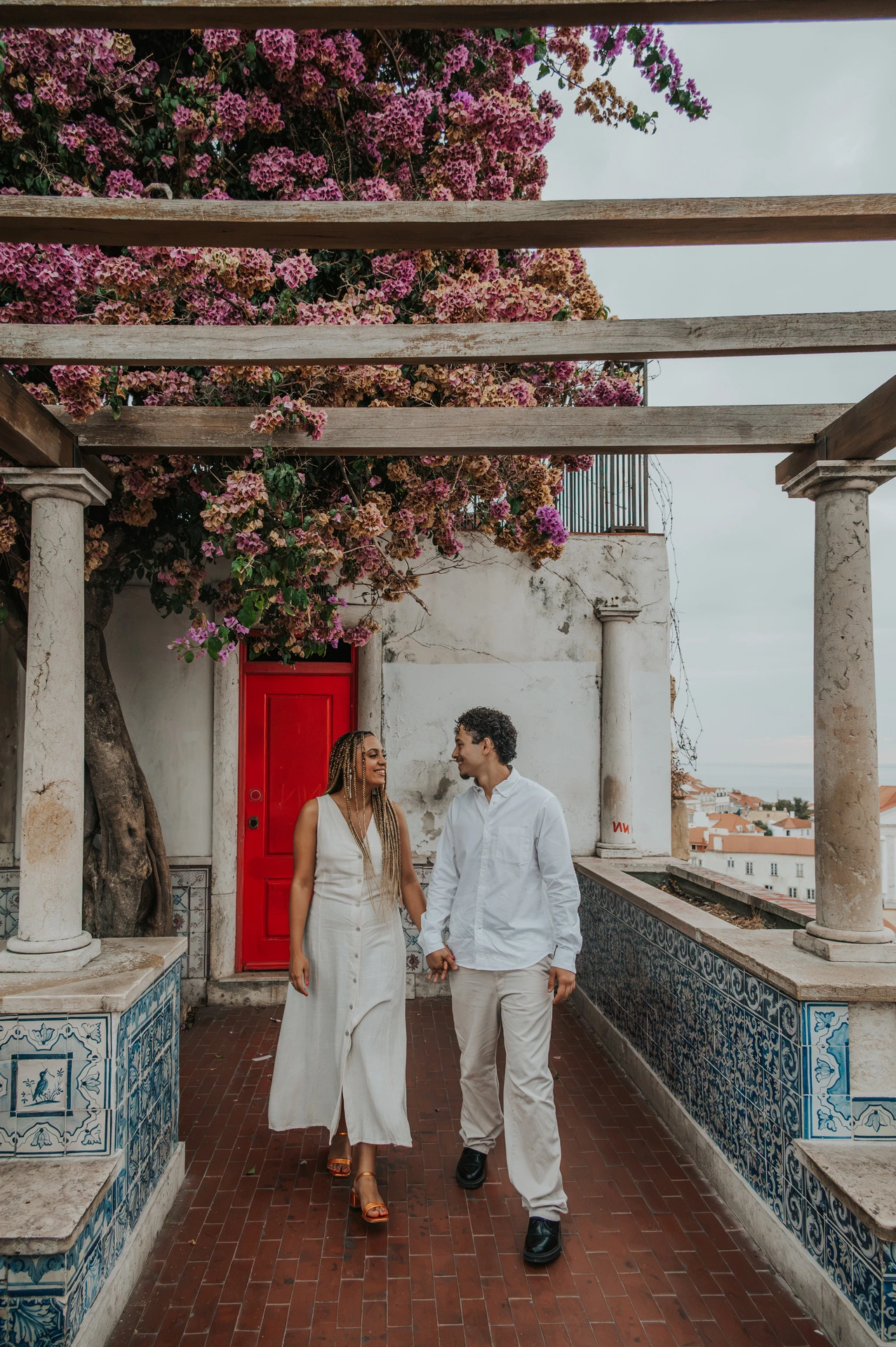 The couple holding hands beneath the garden pergola beside Portuguese tiles during their couple photoshoot in Lisbon.