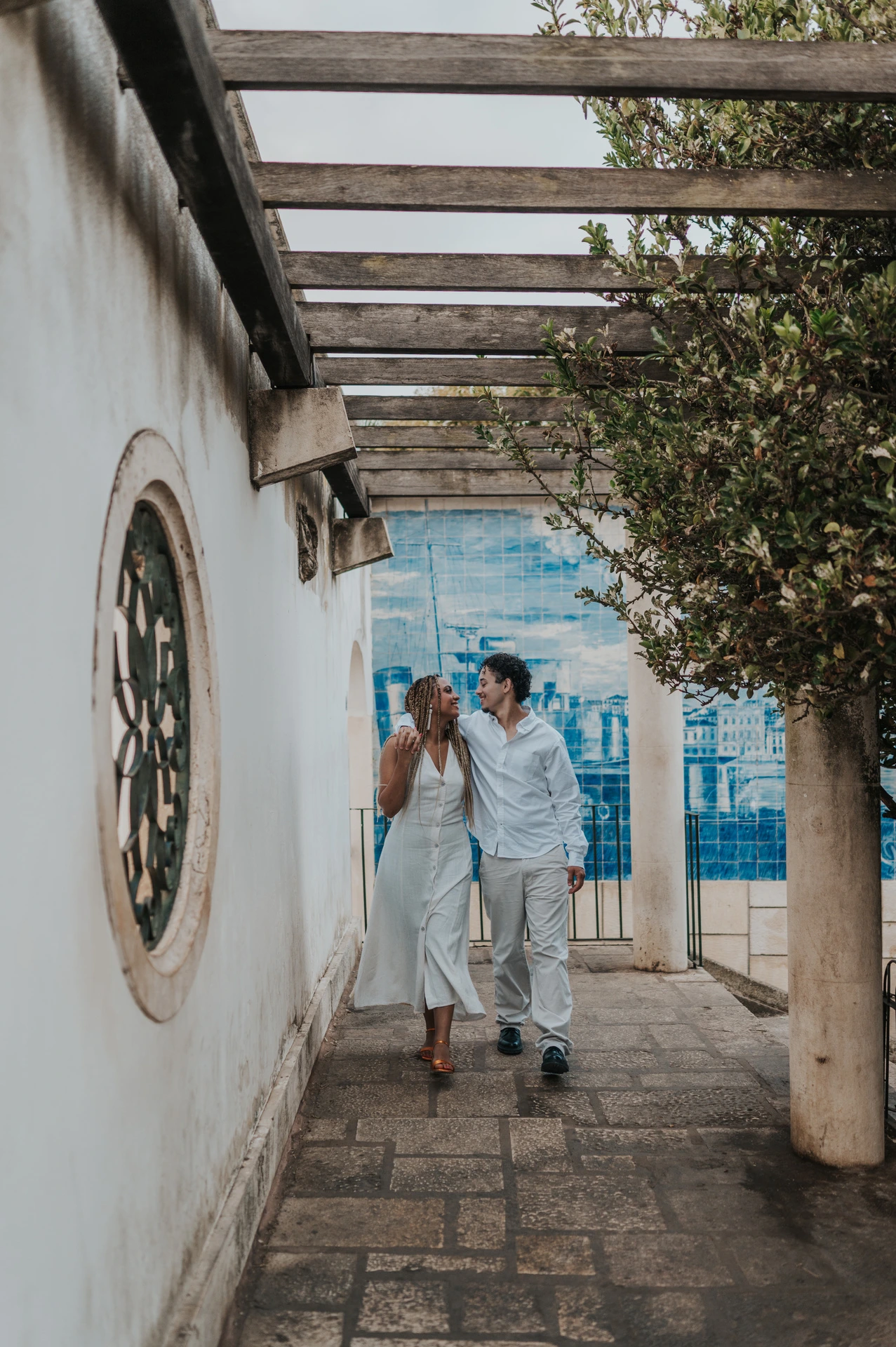 The couple holding hands beneath the garden pergola beside Portuguese tiles during their couple photoshoot in Lisbon.