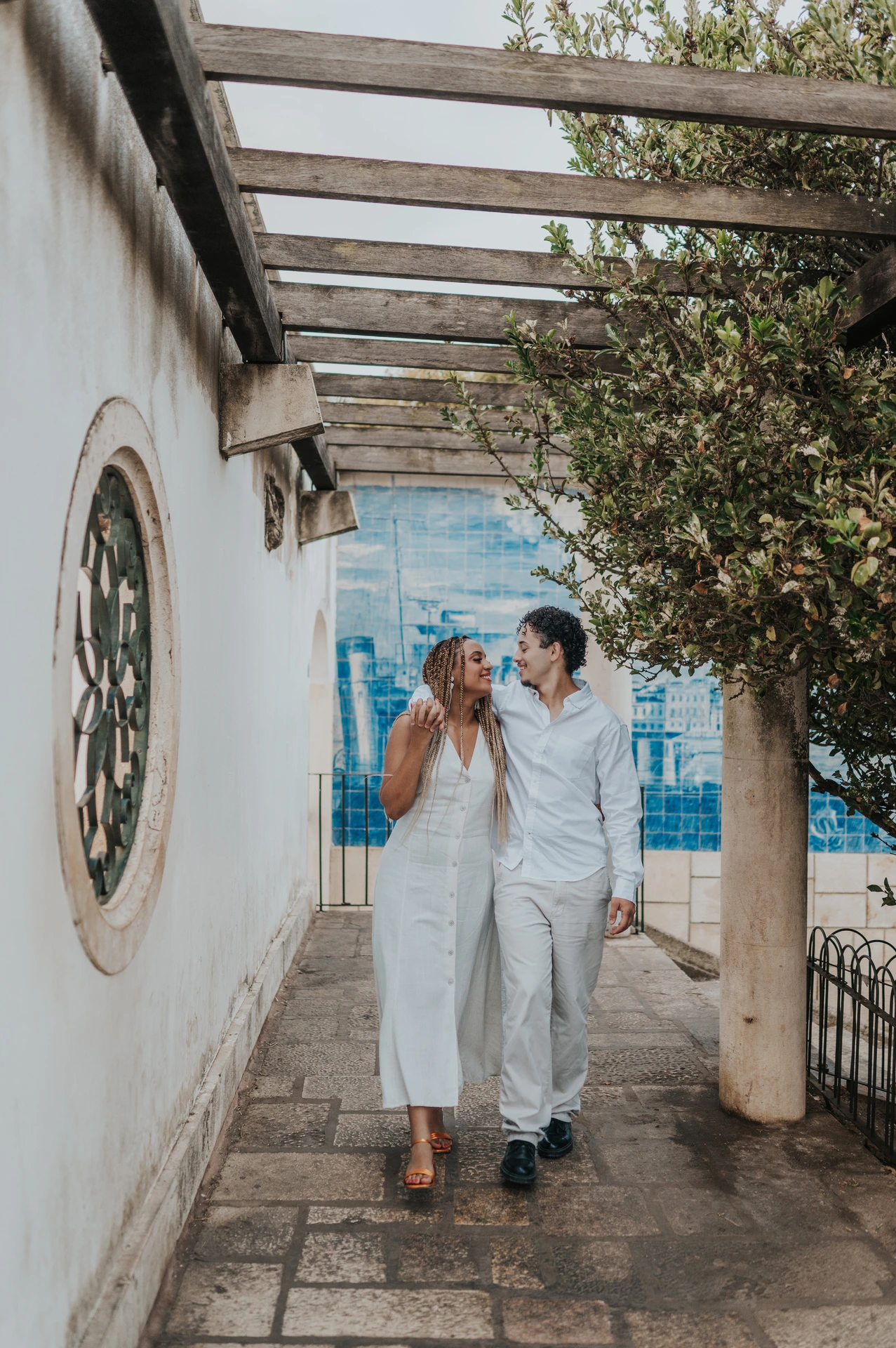 The couple holding hands beneath the garden pergola beside Portuguese tiles during their couple photoshoot in Lisbon.