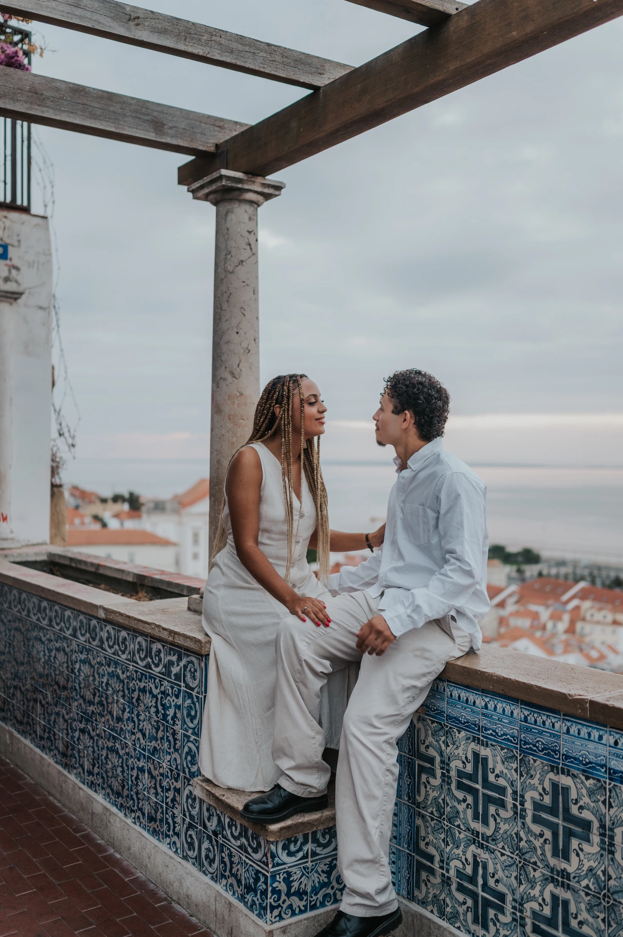 The couple seated facing each other on the tiled wall beneath the pergola during their couple photoshoot in Lisbon.