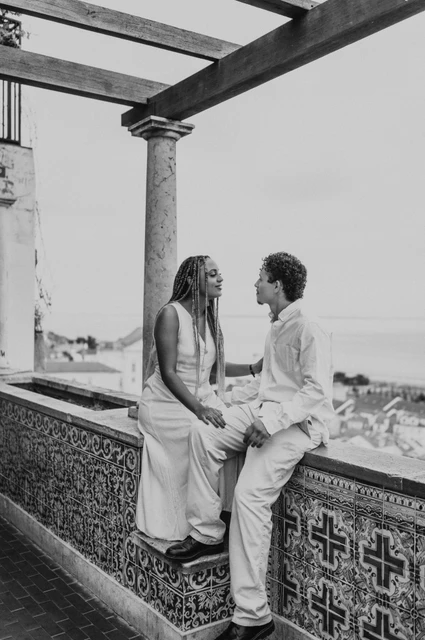 A seated portrait beneath the pergola in black and white | Lisbon couple photoshoot Black-and-white photograph: the couple seated facing each other on the tiled wall beneath the pergola during their couple photoshoot in Lisbon.