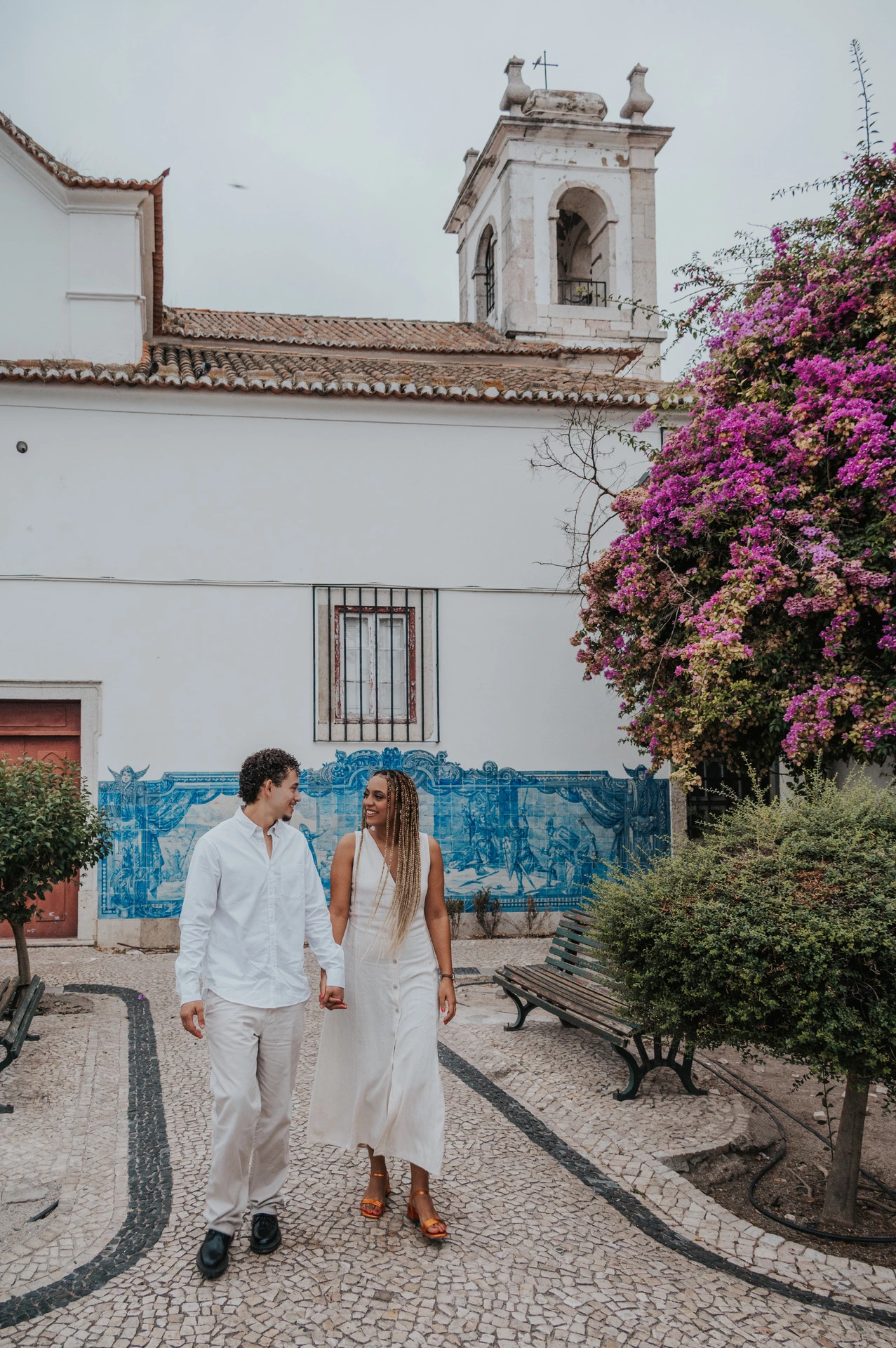 The couple holding hands along the garden path by Igreja de Santa Luzia and its blue tile panels during their couple photoshoot in Lisbon.