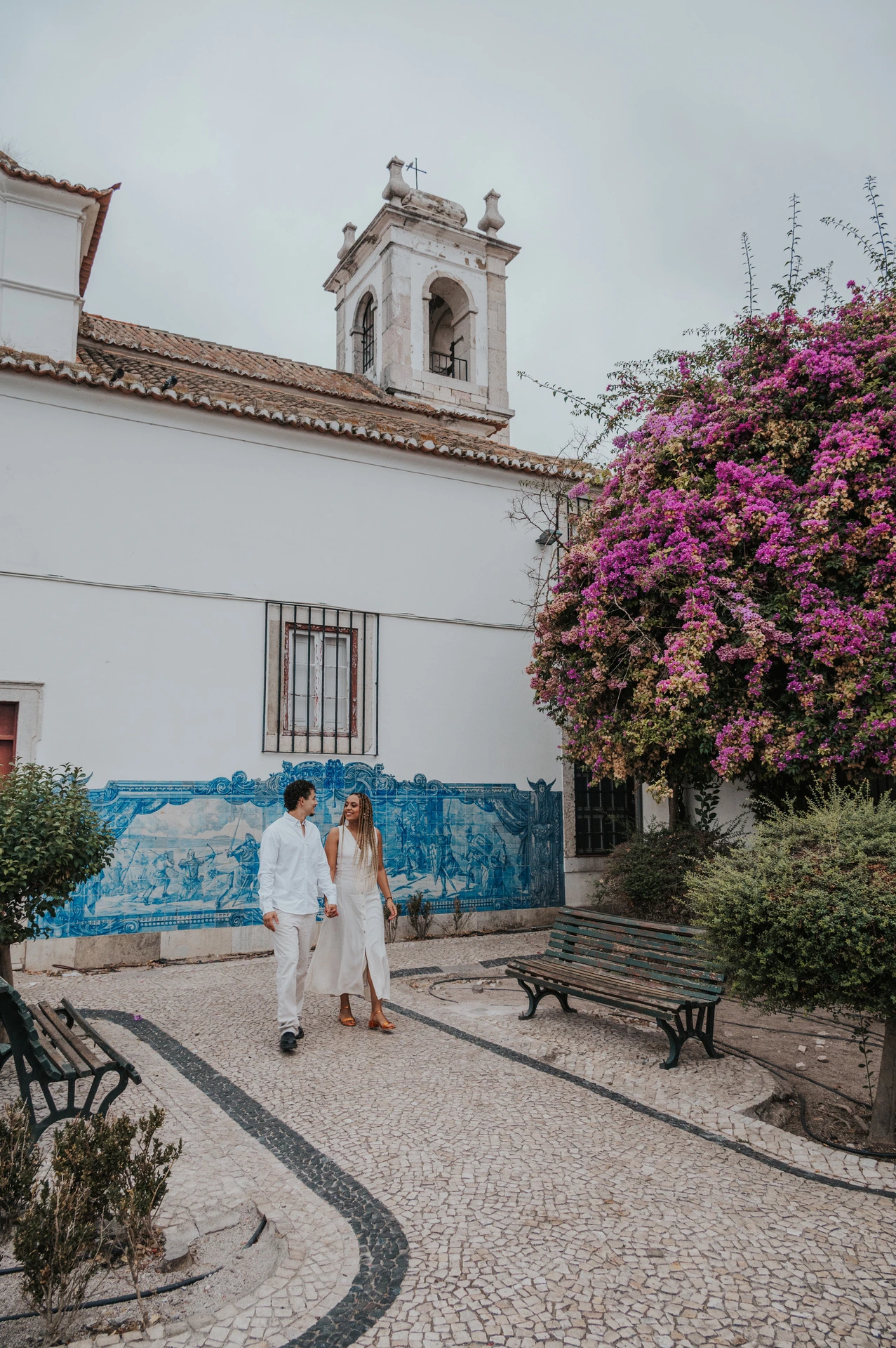 The couple holding hands along the garden path by Igreja de Santa Luzia and its blue tile panels during their couple photoshoot in Lisbon.