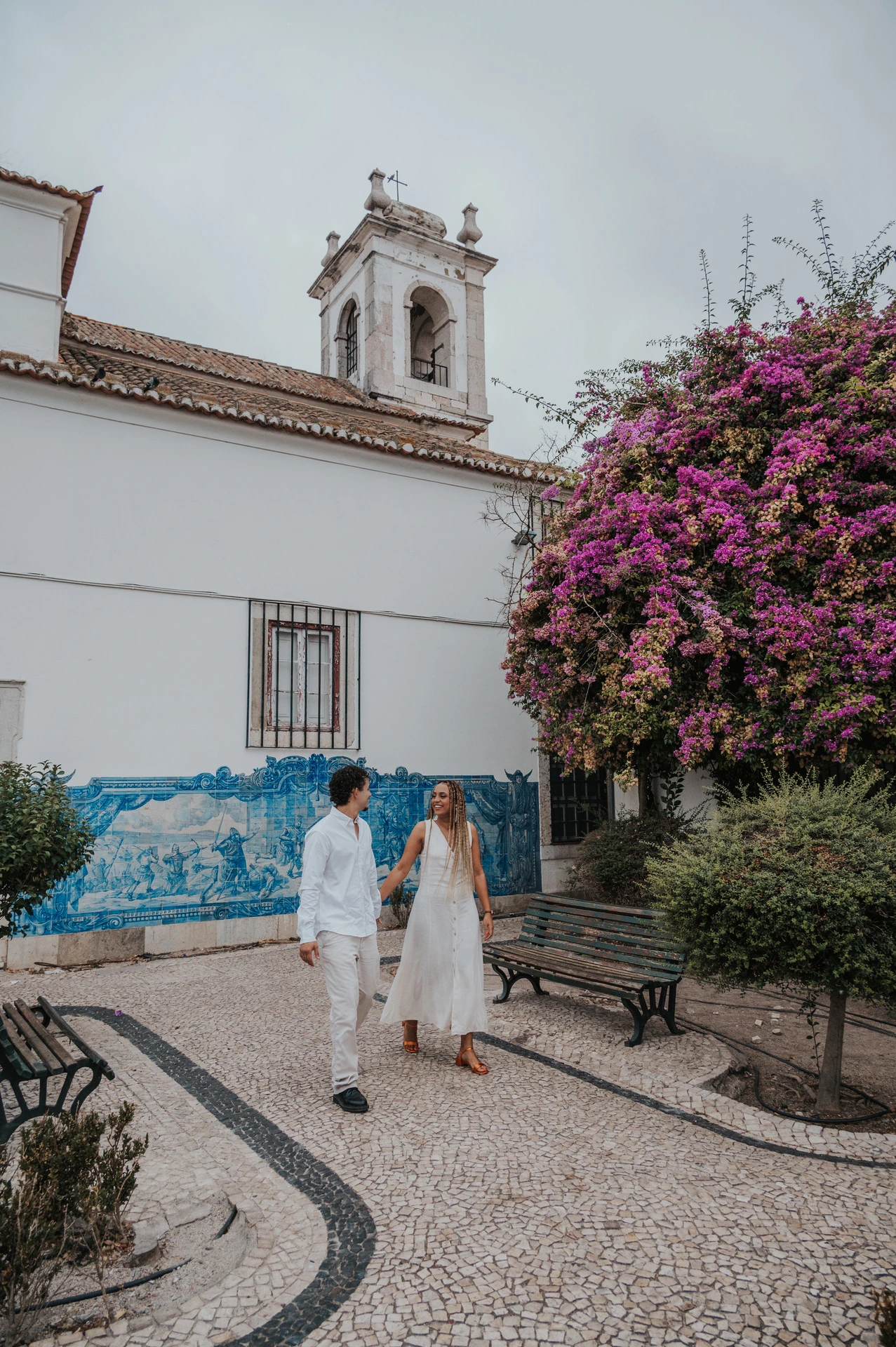 The couple holding hands along the garden path by Igreja de Santa Luzia and its blue tile panels during their couple photoshoot in Lisbon.
