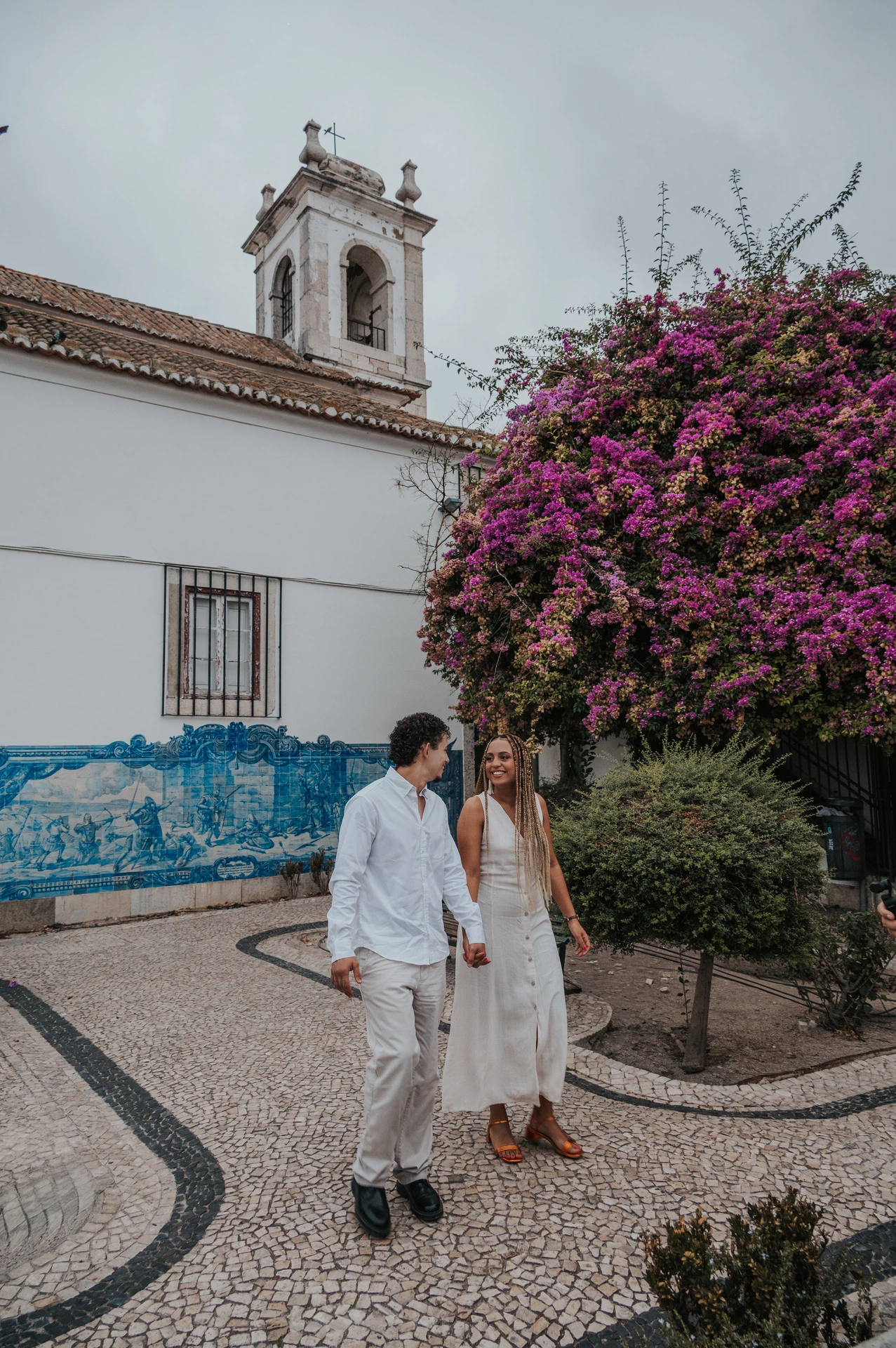 The couple holding hands along the garden path by Igreja de Santa Luzia and its blue tile panels during their couple photoshoot in Lisbon.