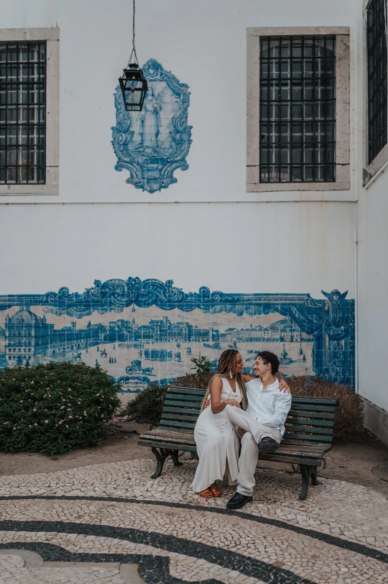 The couple seated close together on a bench in front of the blue tiles at Santa Luzia during their couple photoshoot in Lisbon.