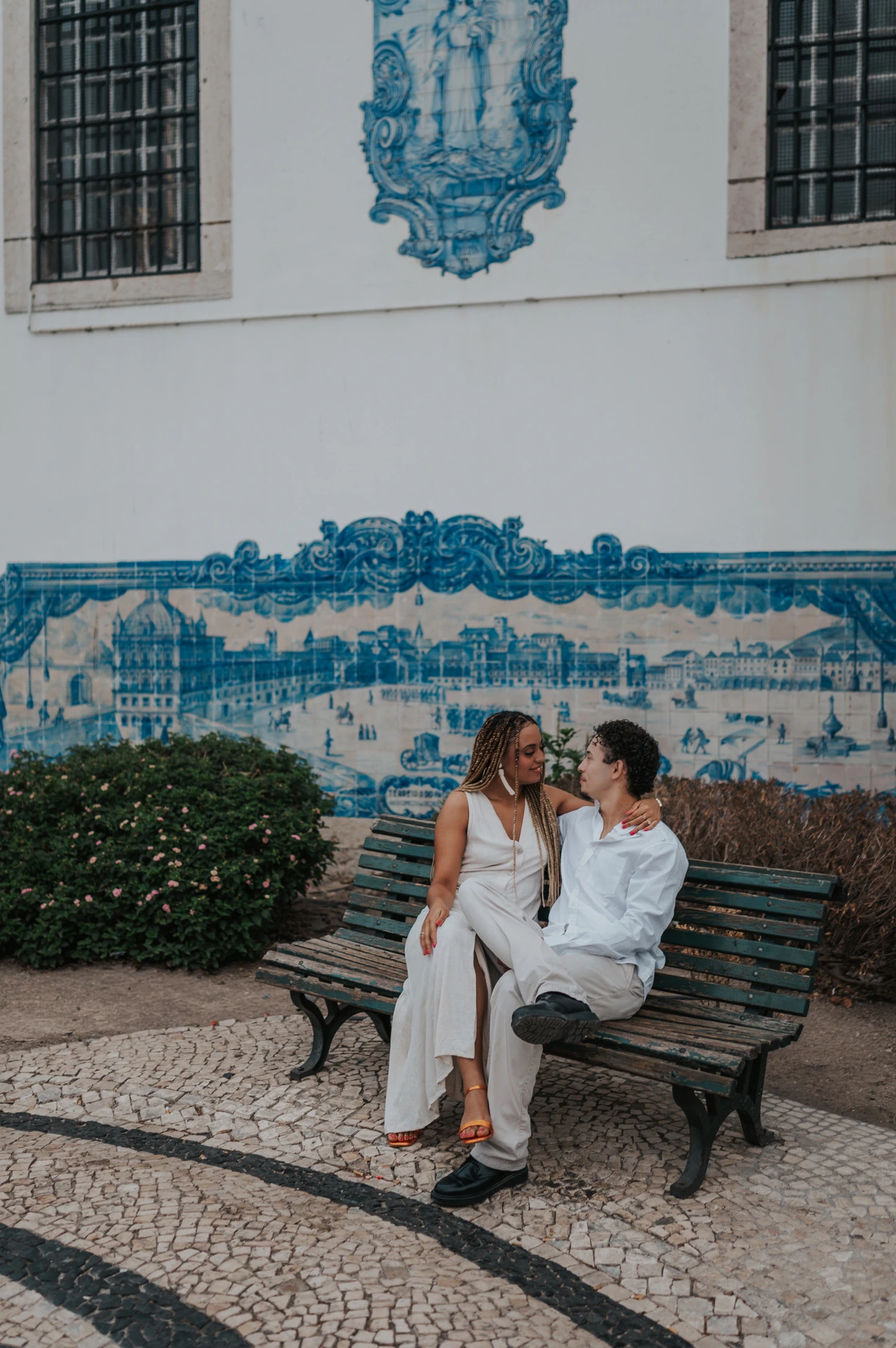 The couple seated close together on a bench in front of the blue tiles at Santa Luzia during their couple photoshoot in Lisbon.
