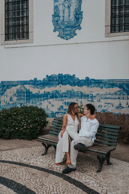 Close together beside the blue tiles | Lisbon couple photoshoot The couple seated close together on a bench in front of the blue tiles at Santa Luzia during their couple photoshoot in Lisbon.