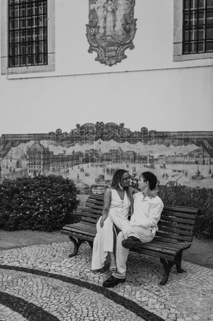 Close together beside the blue tiles in black and white | Lisbon couple photoshoot Black-and-white photograph: the couple seated close together on a bench in front of the blue tiles at Santa Luzia during their couple photoshoot in Lisbon.