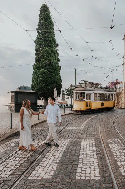 A street walk beside the yellow tram | Lisbon couple photoshoot The couple walking together beside the curved tram tracks with a yellow tram in the background during their couple photoshoot in Lisbon.