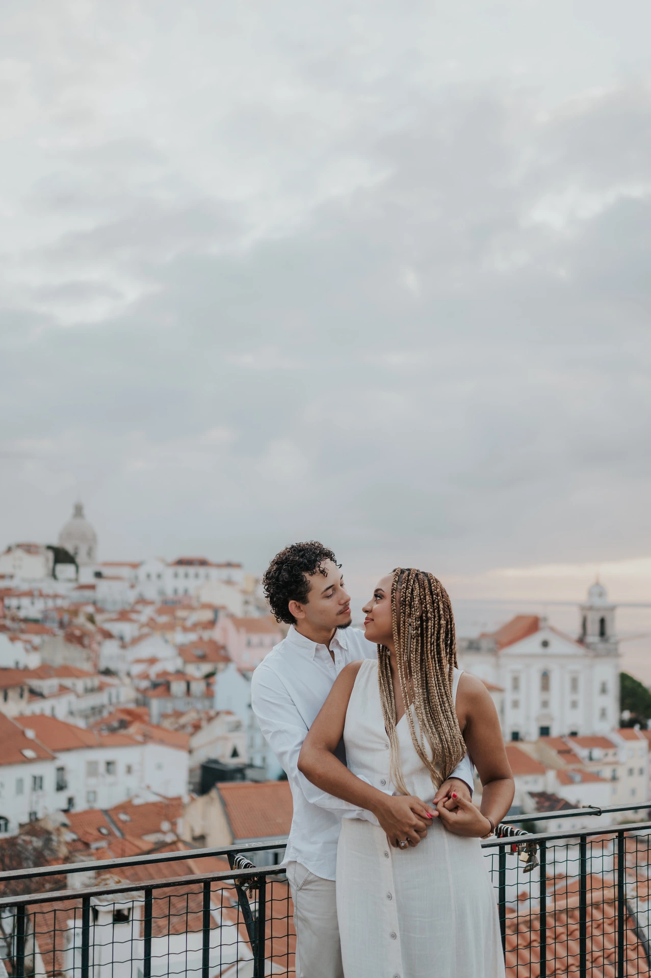 The man embracing his partner with the red rooftops and water behind them at the viewpoint during their couple photoshoot in Lisbon.