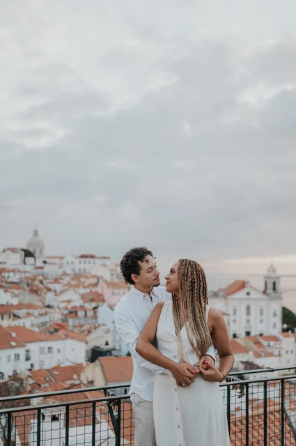 An embrace above the city | Lisbon couple photoshoot The man embracing his partner with the red rooftops and water behind them at the viewpoint during their couple photoshoot in Lisbon.