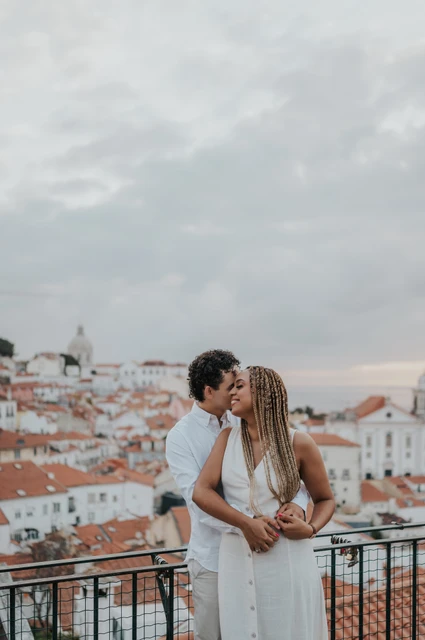 An embrace above the city | Lisbon couple photoshoot The man embracing his partner with the red rooftops and water behind them at the viewpoint during their couple photoshoot in Lisbon.