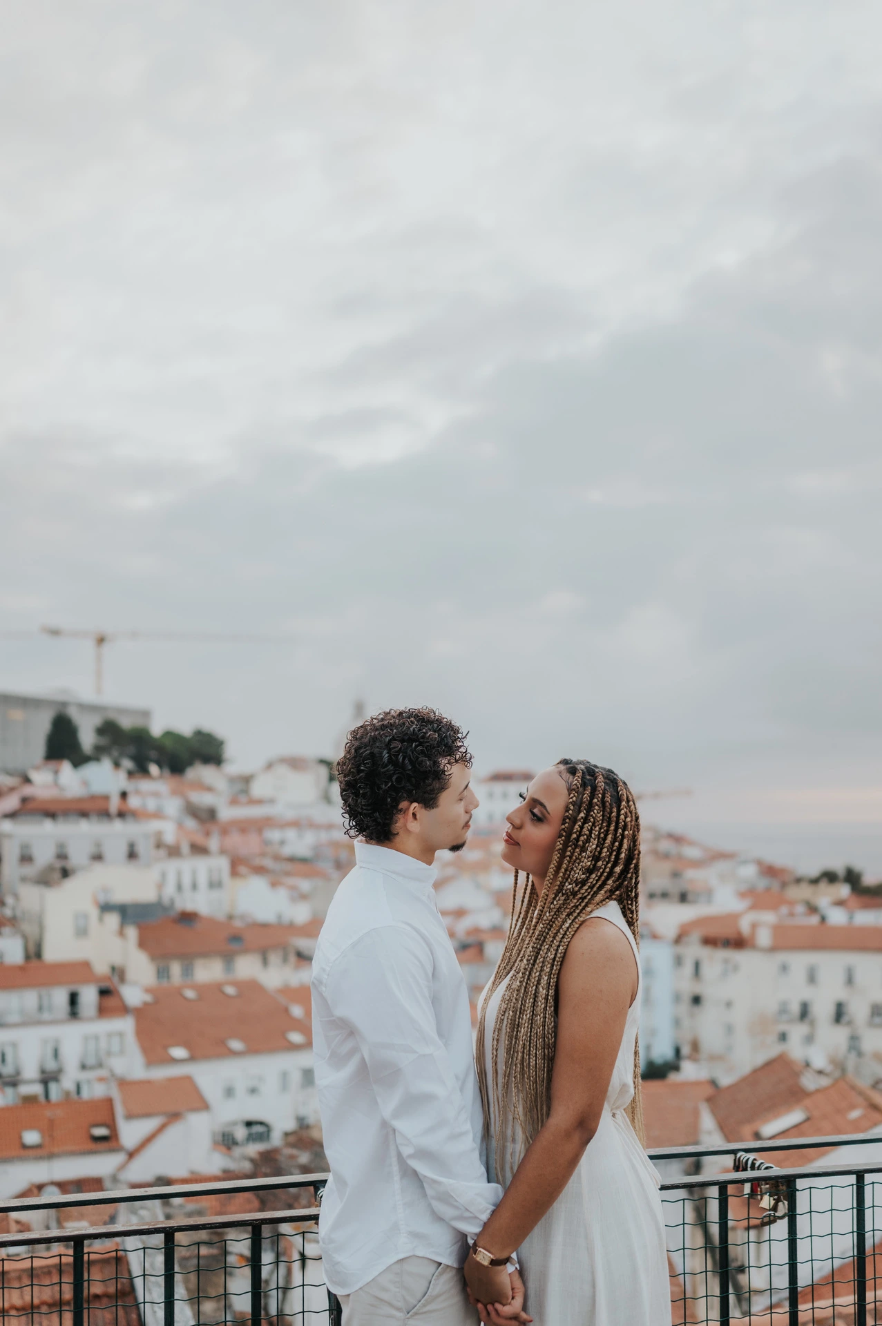 The man embracing his partner with the red rooftops and water behind them at the viewpoint during their couple photoshoot in Lisbon.