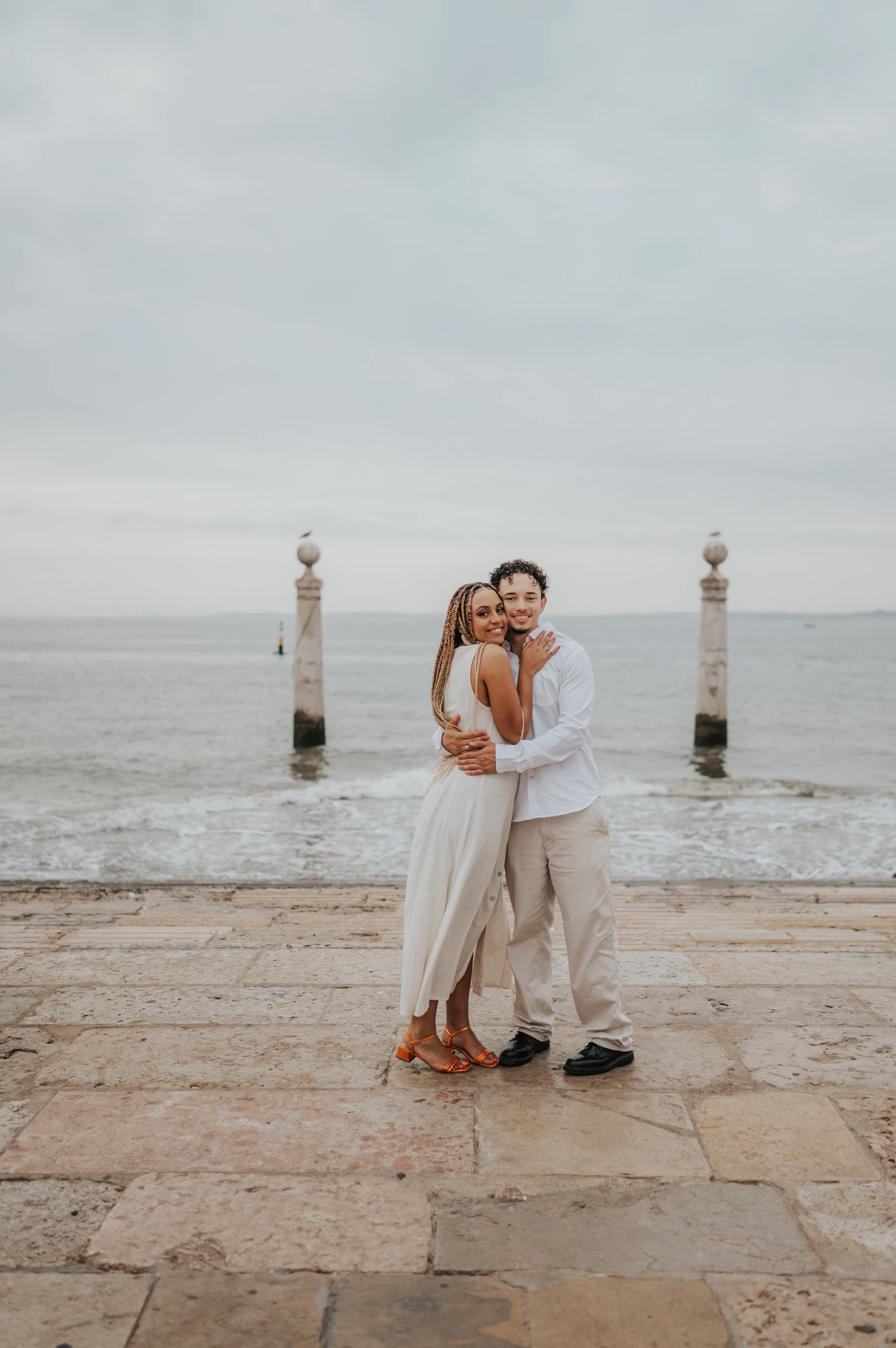 The couple standing close together on the waterfront steps with the river behind them during their couple photoshoot in Lisbon.