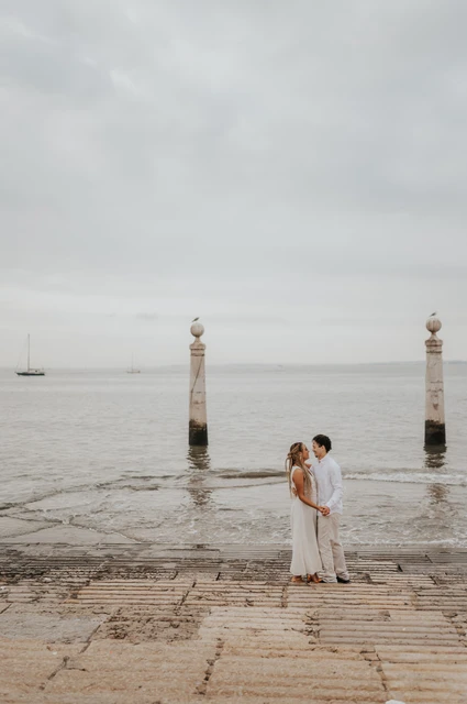 A kiss beside the Tagus River | Lisbon couple photoshoot The couple kissing on the waterfront steps with the river and two stone columns behind them during their couple photoshoot in Lisbon.